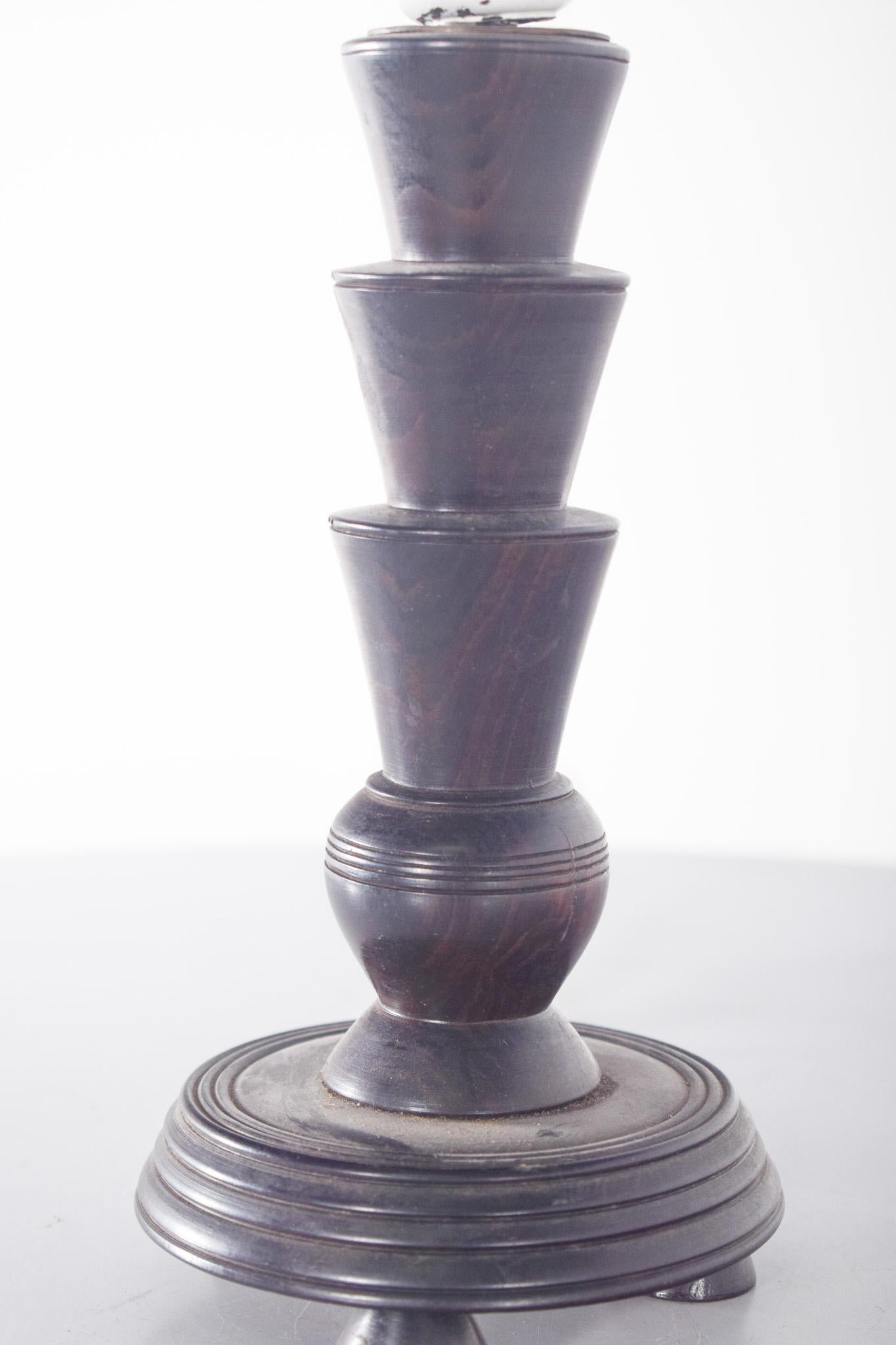 Table lamp, made of wood. With a sculptural and geometric design, characterized by a succession of conical shapes cut and stacked in the shape of a column, it creates a dynamic visual effect.
The circular base rests on three small turned feet and