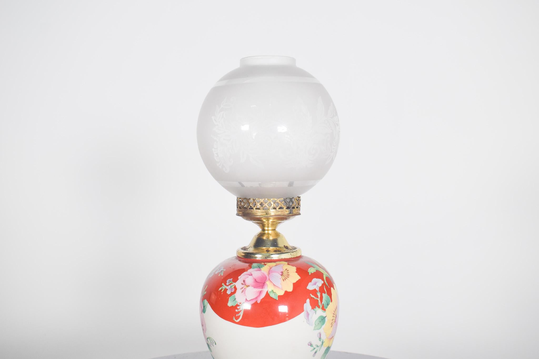 Lampe de table du milieu du siècle. Avec base et embout en métal, corps en céramique avec décoration florale polychrome et abat-jour en verre en forme de boule.
La base de la lampe a une forme de vase arrondi et est décorée de fleurs, dans des tons