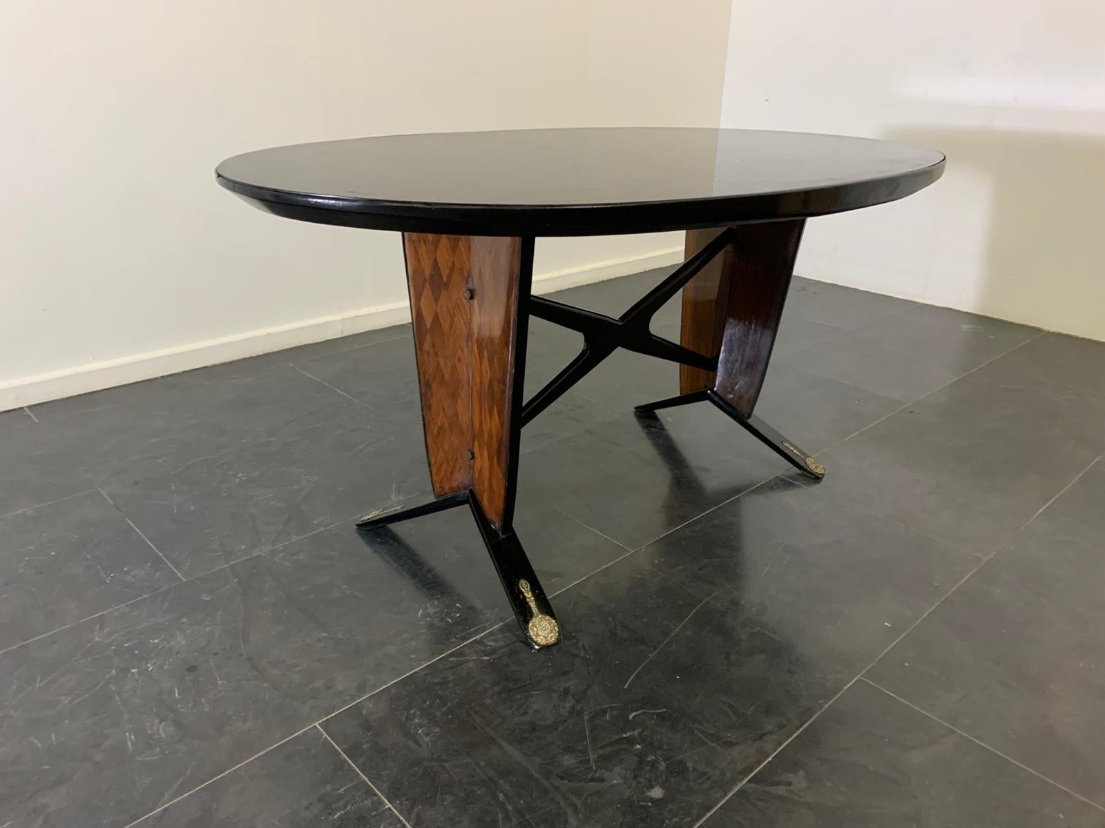 Oval ebonized wood, mahogany and black glass table, 1950s. Under-top cross vault, feet and borders are ebonized. Under the top stands out the finely inlaid rhomboid-patterned base that ends by resting on vertical laths with delightfully rich brass