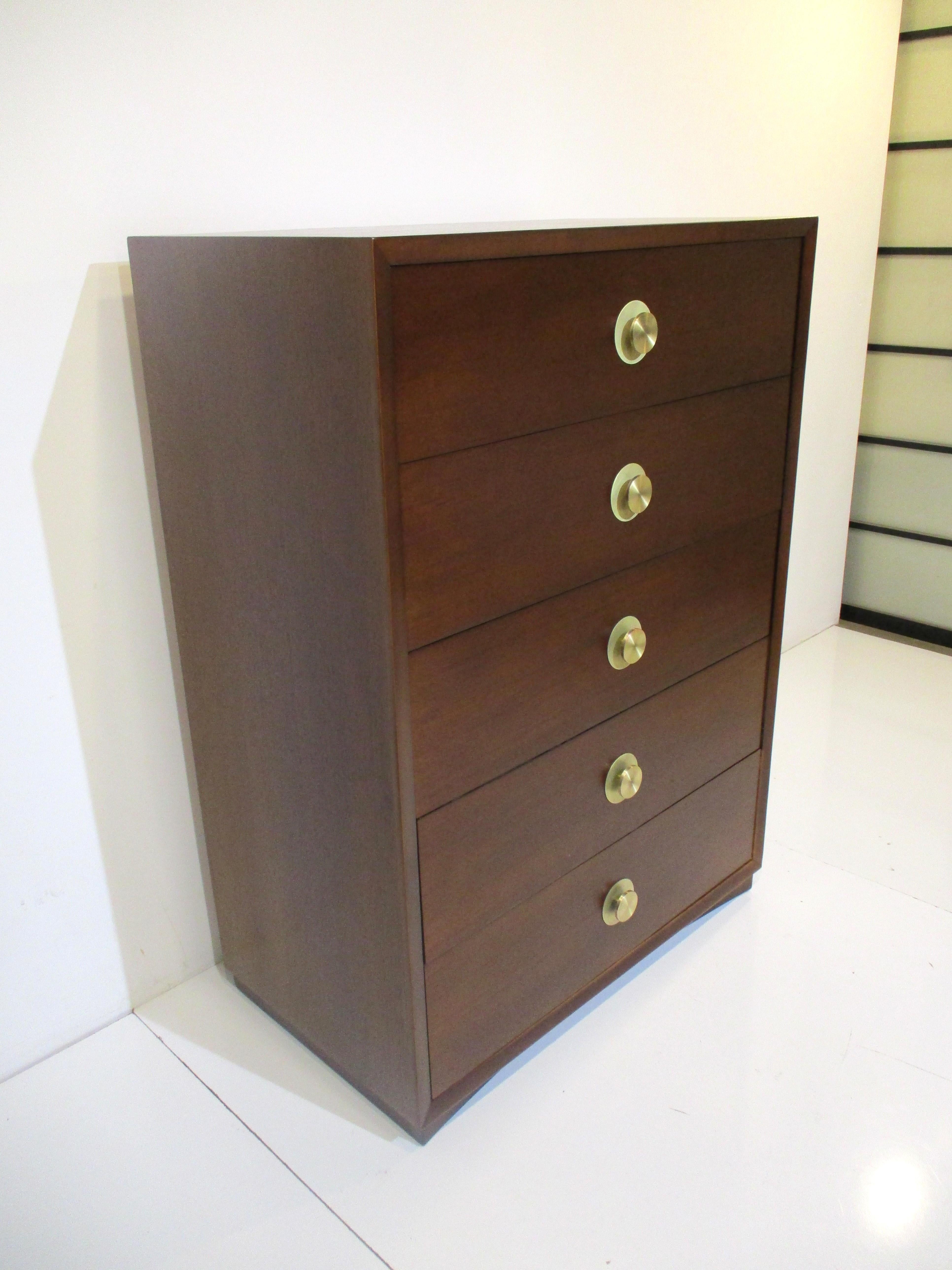 A very well crafted dark walnut toned tall dresser chest with five drawers the top two having dividers. The round brass cast styled pulls with backing plate give the piece a classic look manufactured in the style of the Widdicomb furniture company