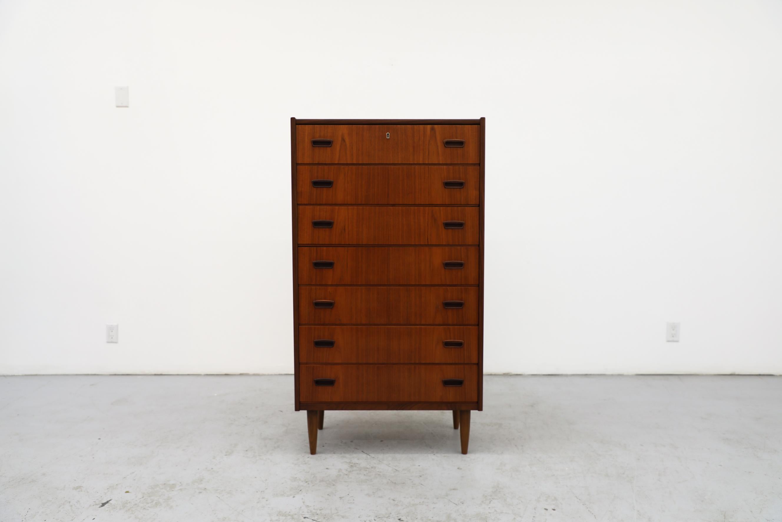 Teak dresser with 7 slender drawers and tapered legs. This piece has been lightly refinished with some remaining visible wear, consistent with its age and use. Missing key.