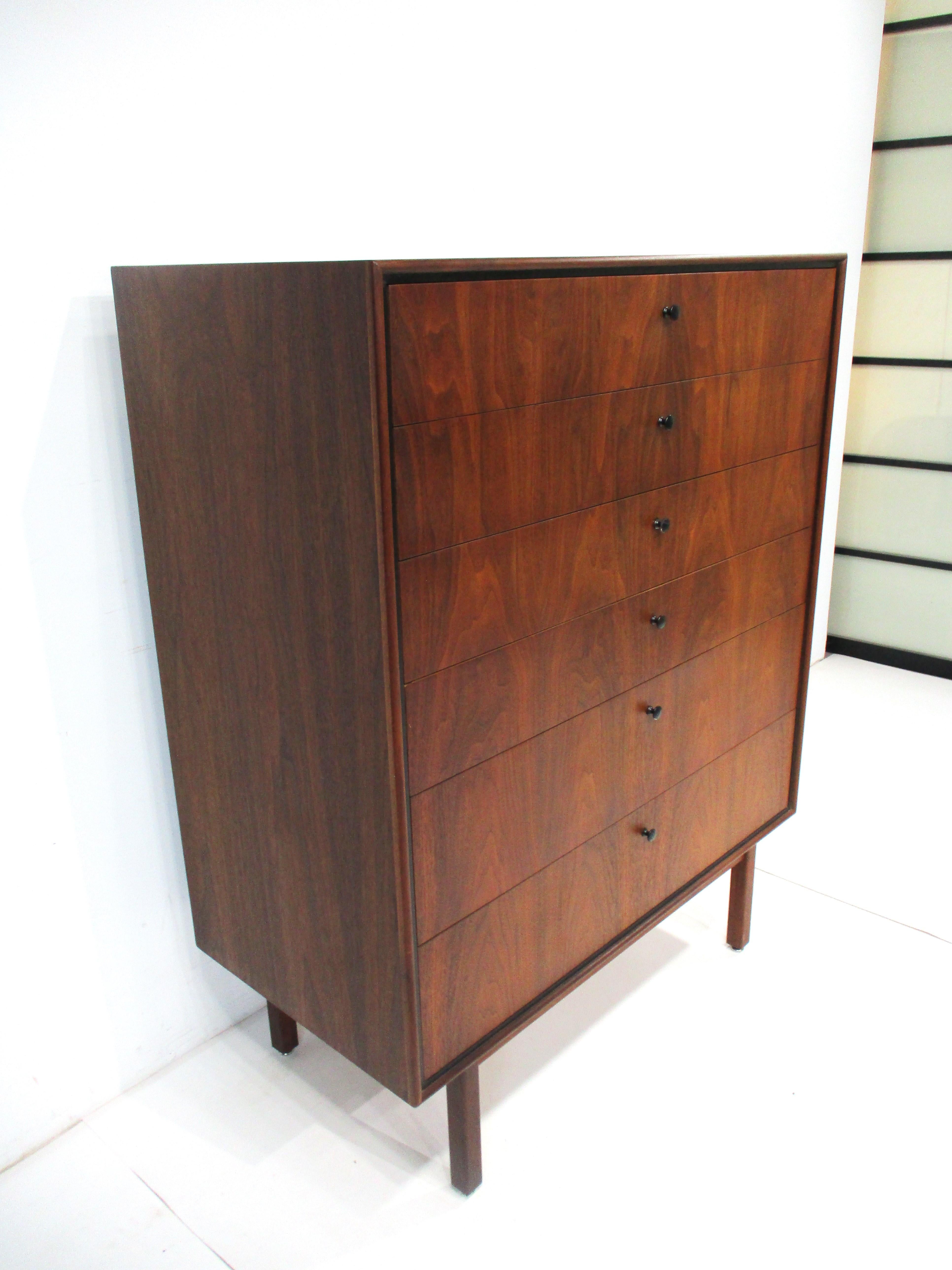 A six drawer Mid Century tall dresser chest in dark rich walnut with fantastic graining to the front and sides having satin black pulls sitting on a matching base . With plenty of functional storage , this would be a statement piece and would