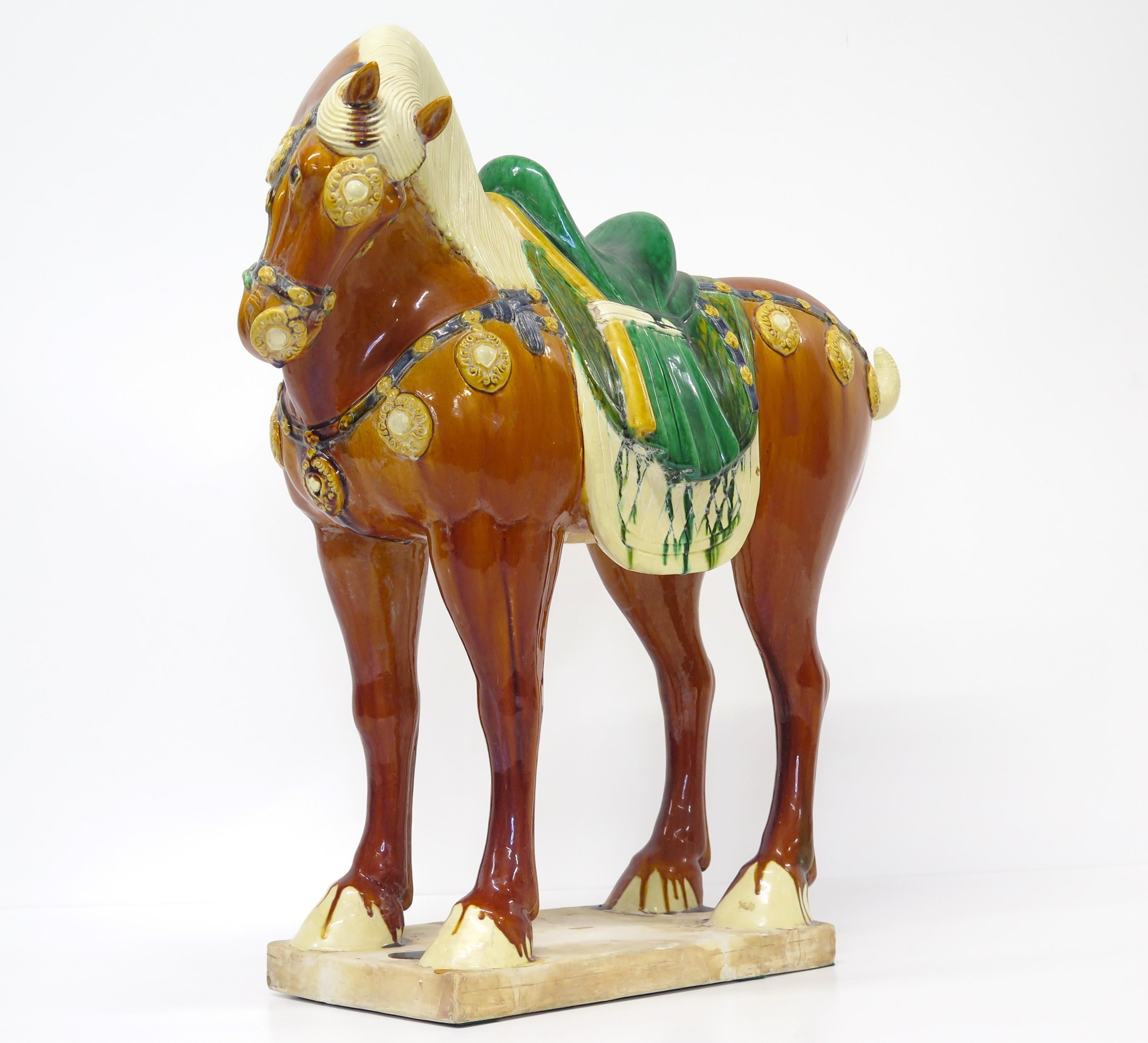 a beautifully modeled glazed Chinese ceramic horse, in the Tang-style, golden brown body with buff mane, removable tail, and hooves with a green saddle and harness with yellow-gold ornaments, mid-20th century, China

firing hairline / crack in the