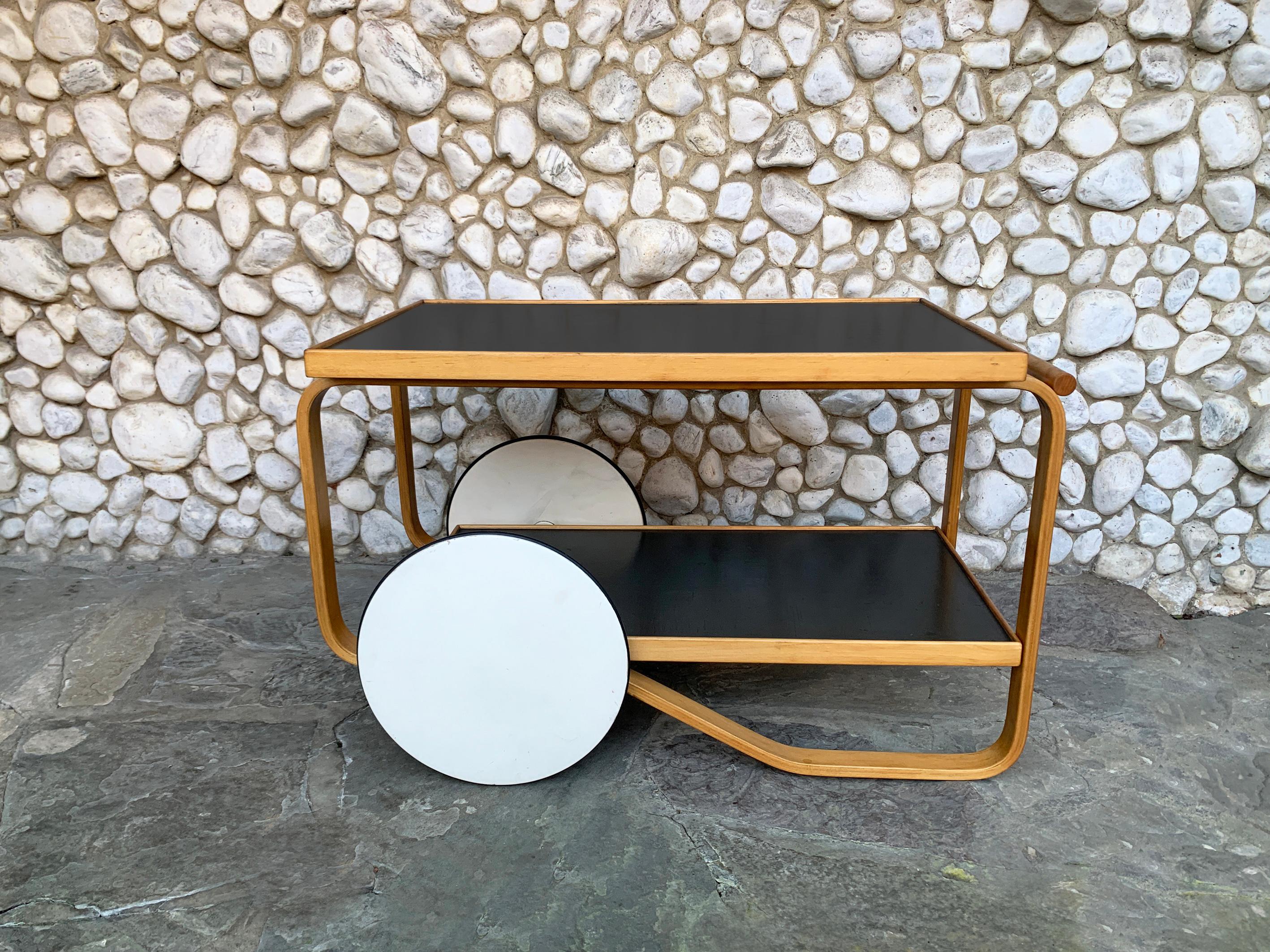 Tea Cart or Trolley model 901 designed by Aino and Alvar Aalto for Artek.
Made in Finland. Manufactured probably in the 1950s.
Birch frame, contrasting shelving with black linoleum, large wooden wheels painted white.

Alvar Aalto created this