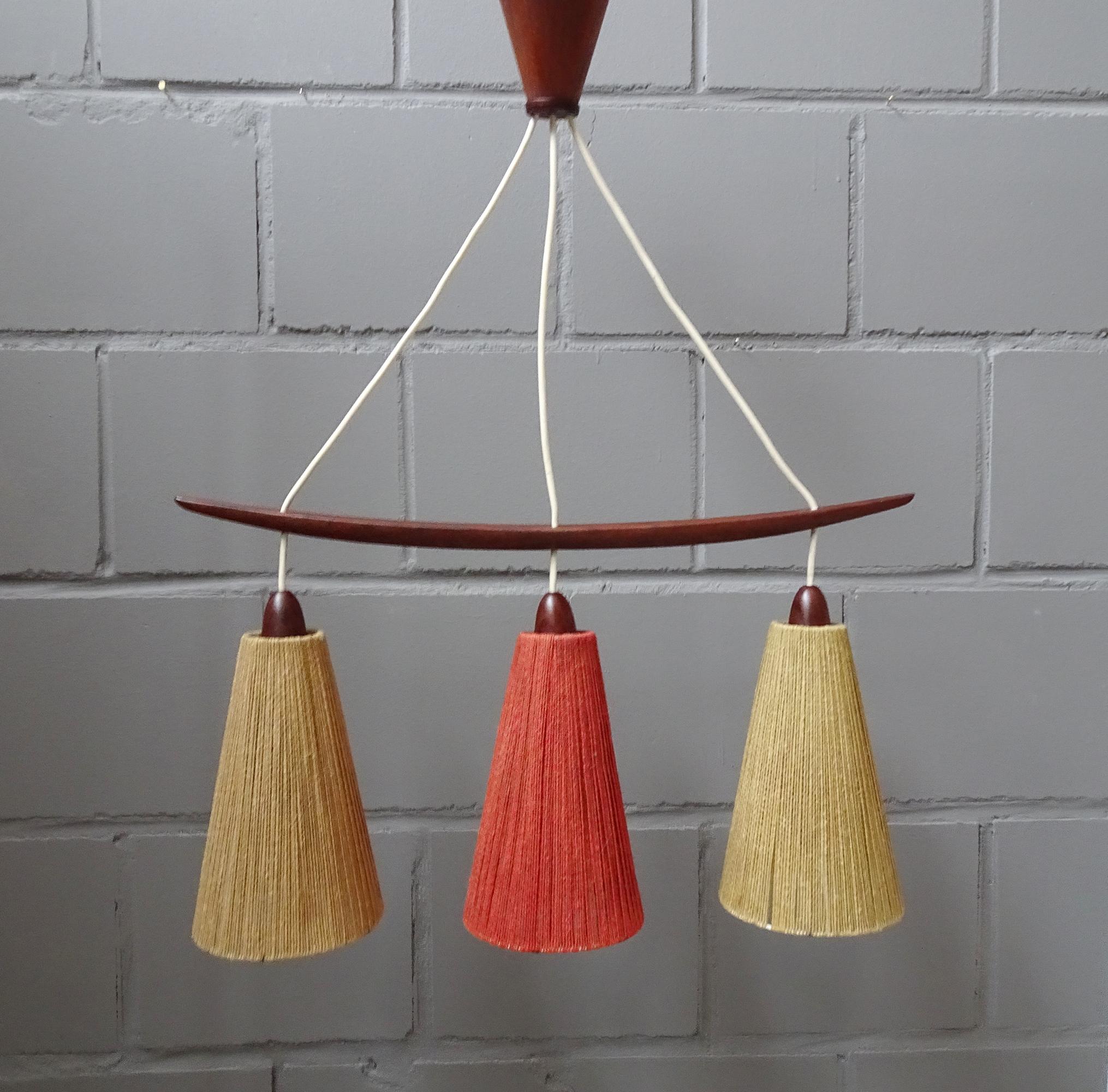 Stylish suspension lamp by Temde from the 1960s. Beautiful midcentury design in high quality workmanship and execution. Three-lamp hanging lamp with lampshades made of metal and a laced cover made of sisal in beige and wine red. The teak details