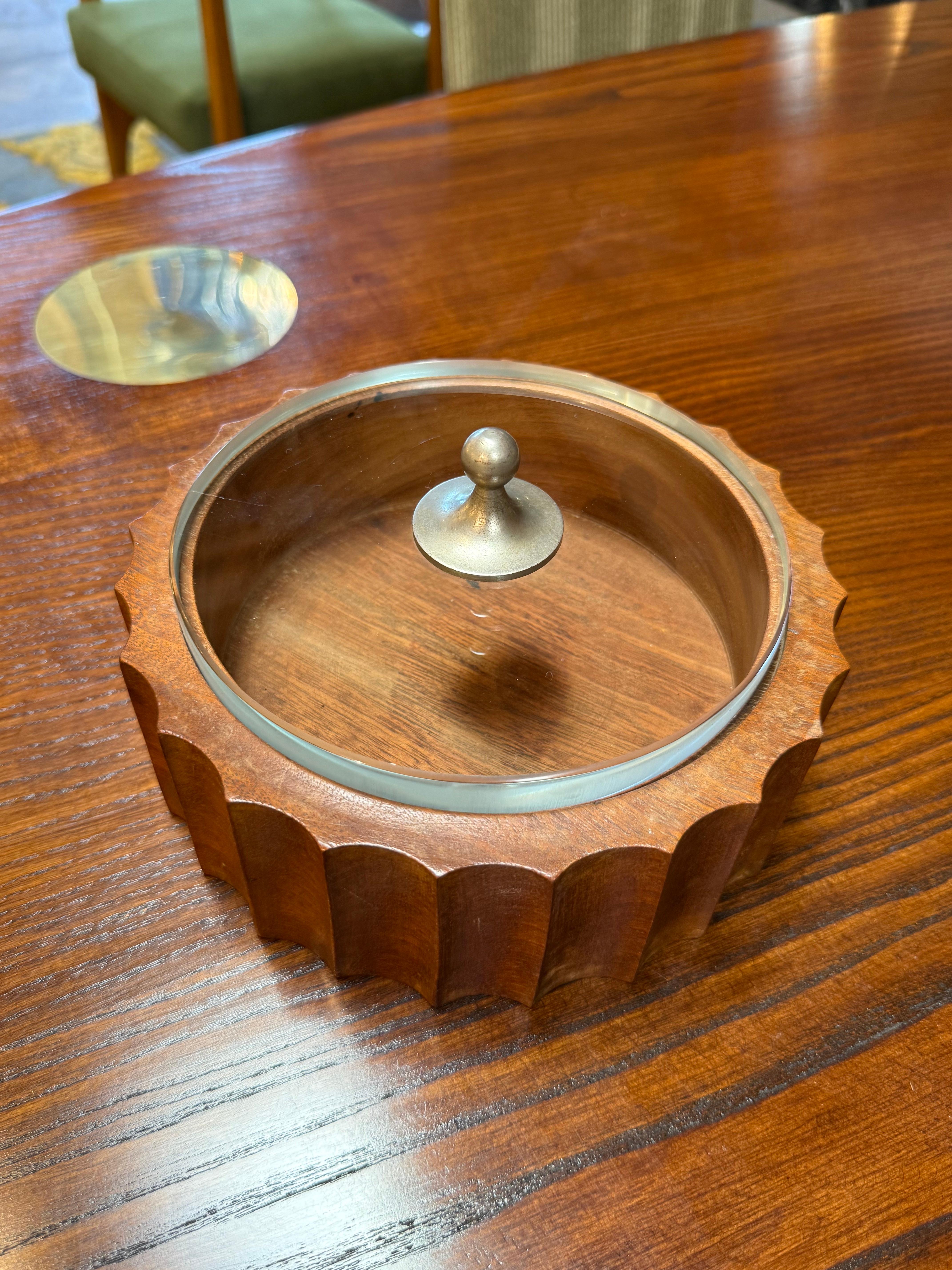 Stylish mid-century modern lidded box crafted from rich teak wood with a scalloped edge design. The piece features a clear glass lid topped with a brass knob, combining warm wood tones with sleek metallic and glass accents. Ideal for use as a