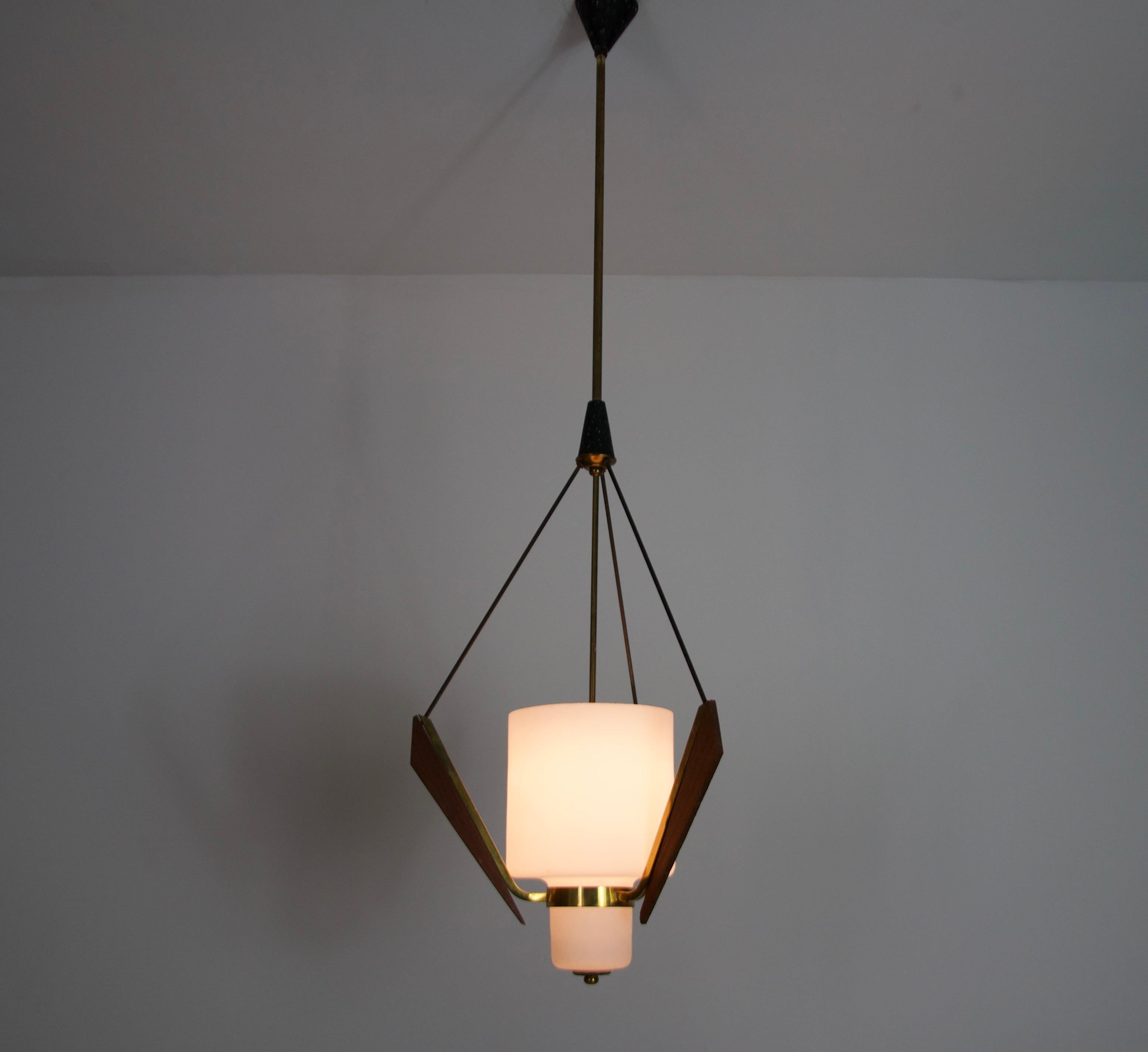 Eleganza scultorea per questa lampada da soffitto del Mid-Century, realizzata negli anni '60 in Italia, che combina magistralmente legno di teak, vetro opalino e dettagli in ottone. Questo lampadario a sospensione, quintessenza del modernismo