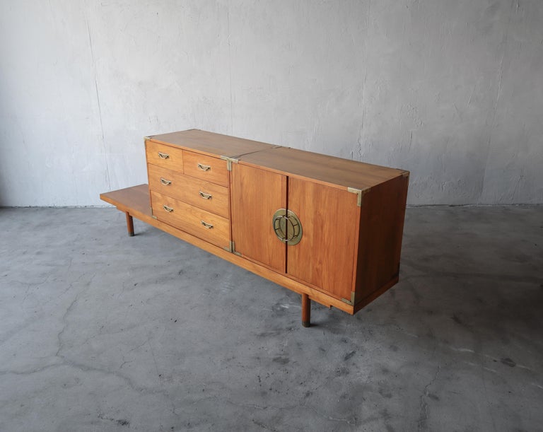 This is a wonderful 3 piece mid century set. An 8.5 ft bench with 2 repositionable cabinets. The set is solid teak construction with very beautiful details, some would say of Asian influence, and amazing brass handles and details. This set would