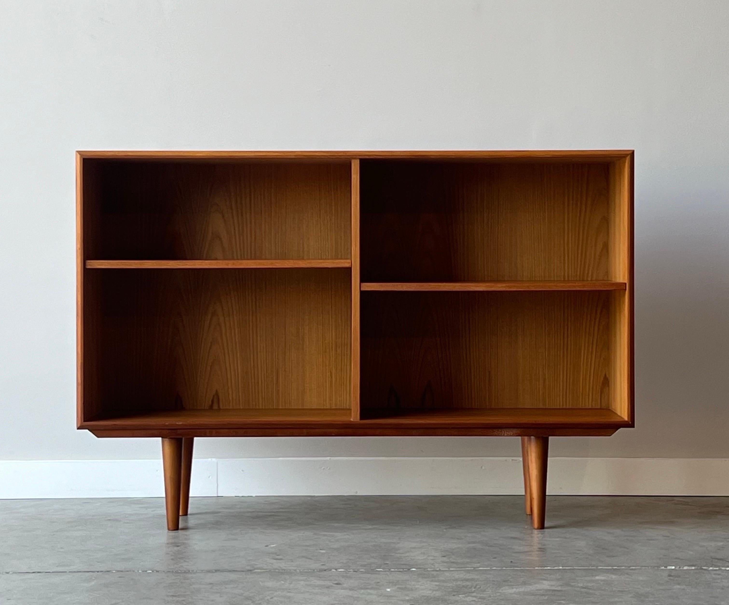 Mid-century Danish teak bookshelf. Quaint and simple with teak case border and two internal teak shelves. Shelves are adjustable. Slim design perfect for small spaces or an entryway. Open face with no glass or doors. Sits on teak tapered legs. In