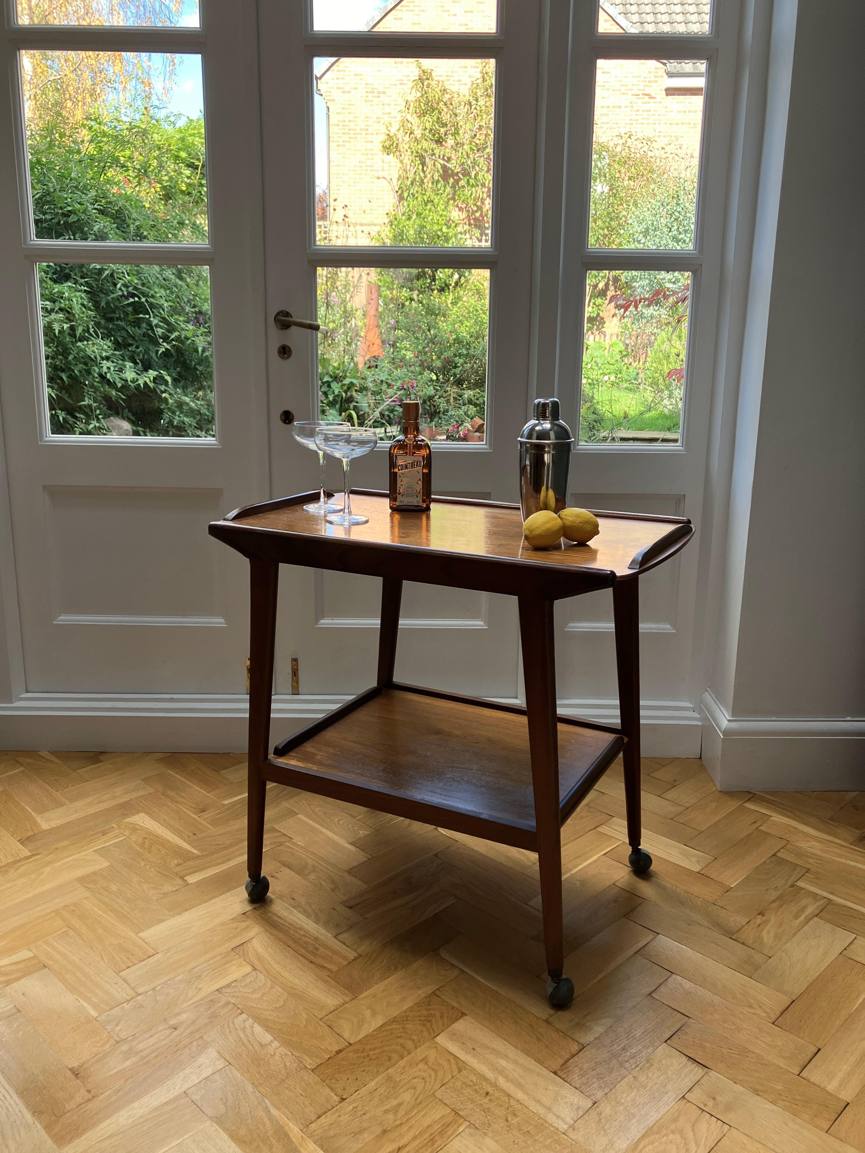 Chariot à boissons classique et moderne du milieu du siècle par Remploy. Le chariot à cocktail comporte deux étages aux proportions et aux formes élégantes. Il a un design épuré et de jolies petites roulettes rondes. Il est fabriqué en teck.