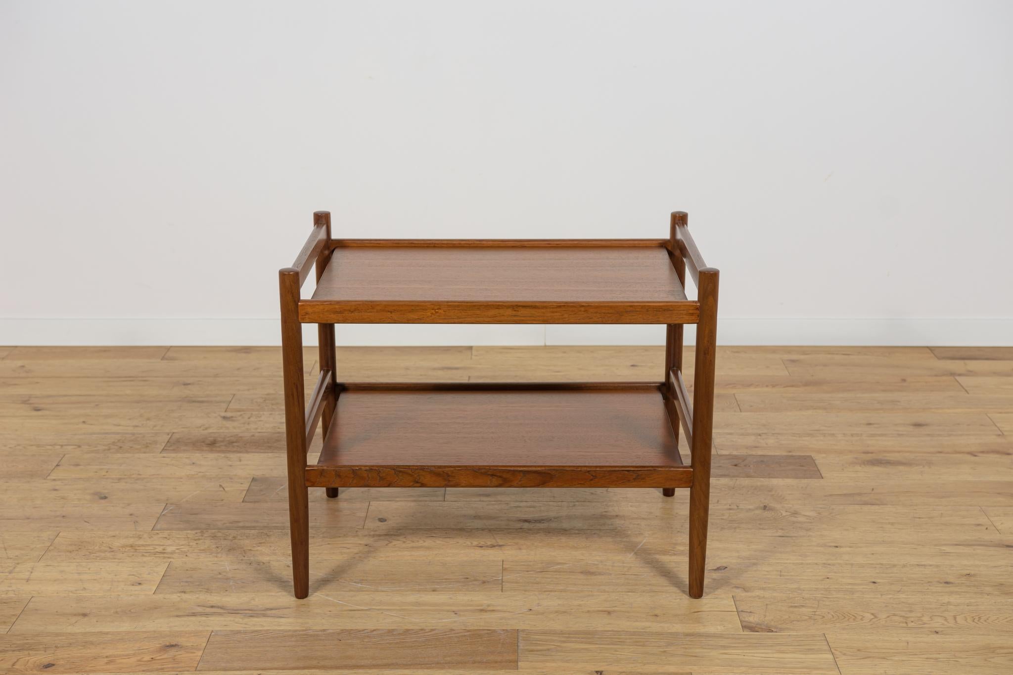 Consola fabricada en Dinamarca en la década de 1970. De teca, con estantes inferiores y superiores. Se ha renovado a fondo, se ha limpiado la madera del antiguo revestimiento, se ha pintado con tinte de roble y se ha acabado con un barniz fuerte