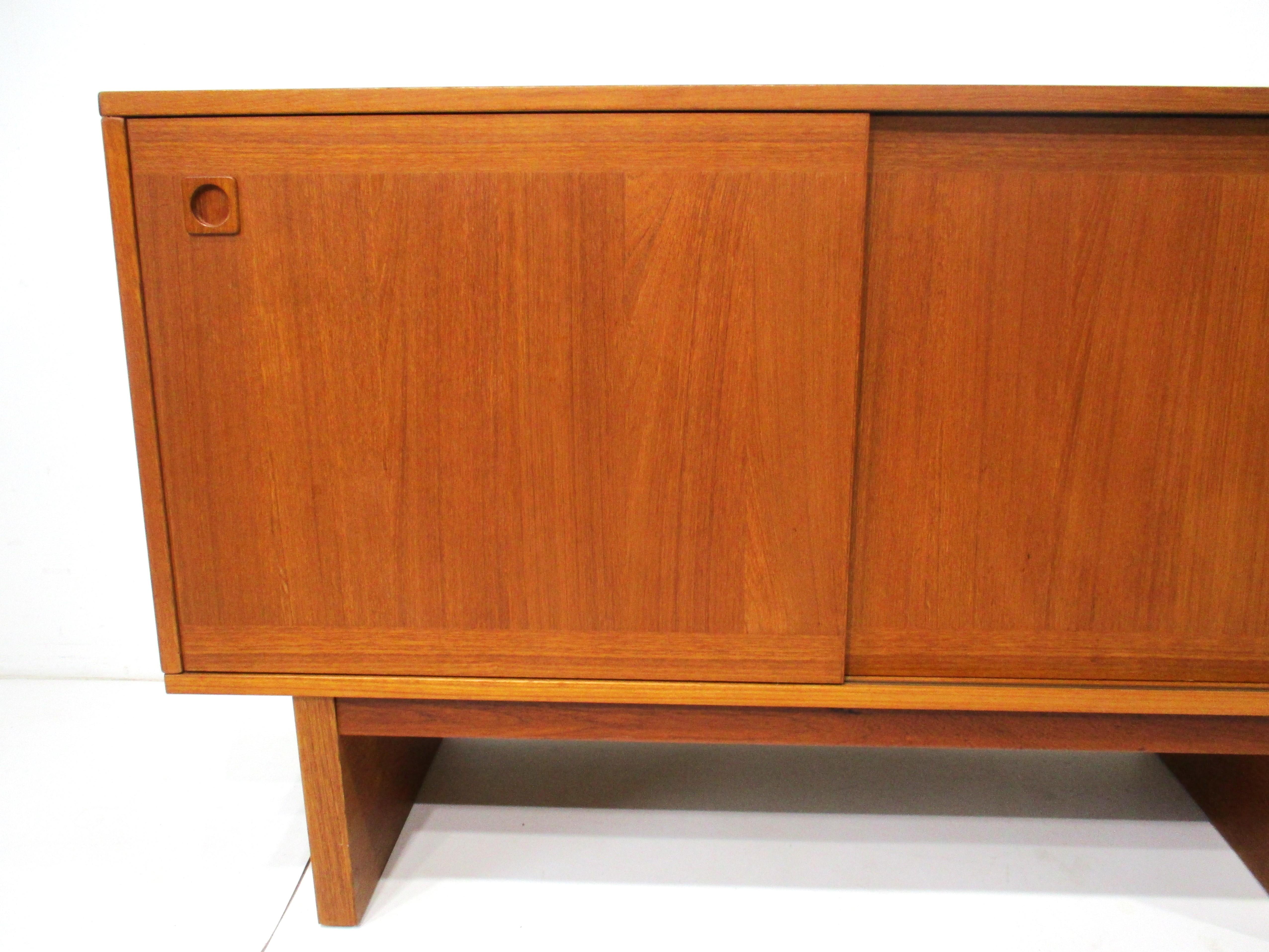 A teak two sliding door credenza with round pulls having two adjustable shelves inside and two drawers . Sitting on matching plinth bases to each end with stretchers making it very sturdy for your stereo and records or use for storage . With the