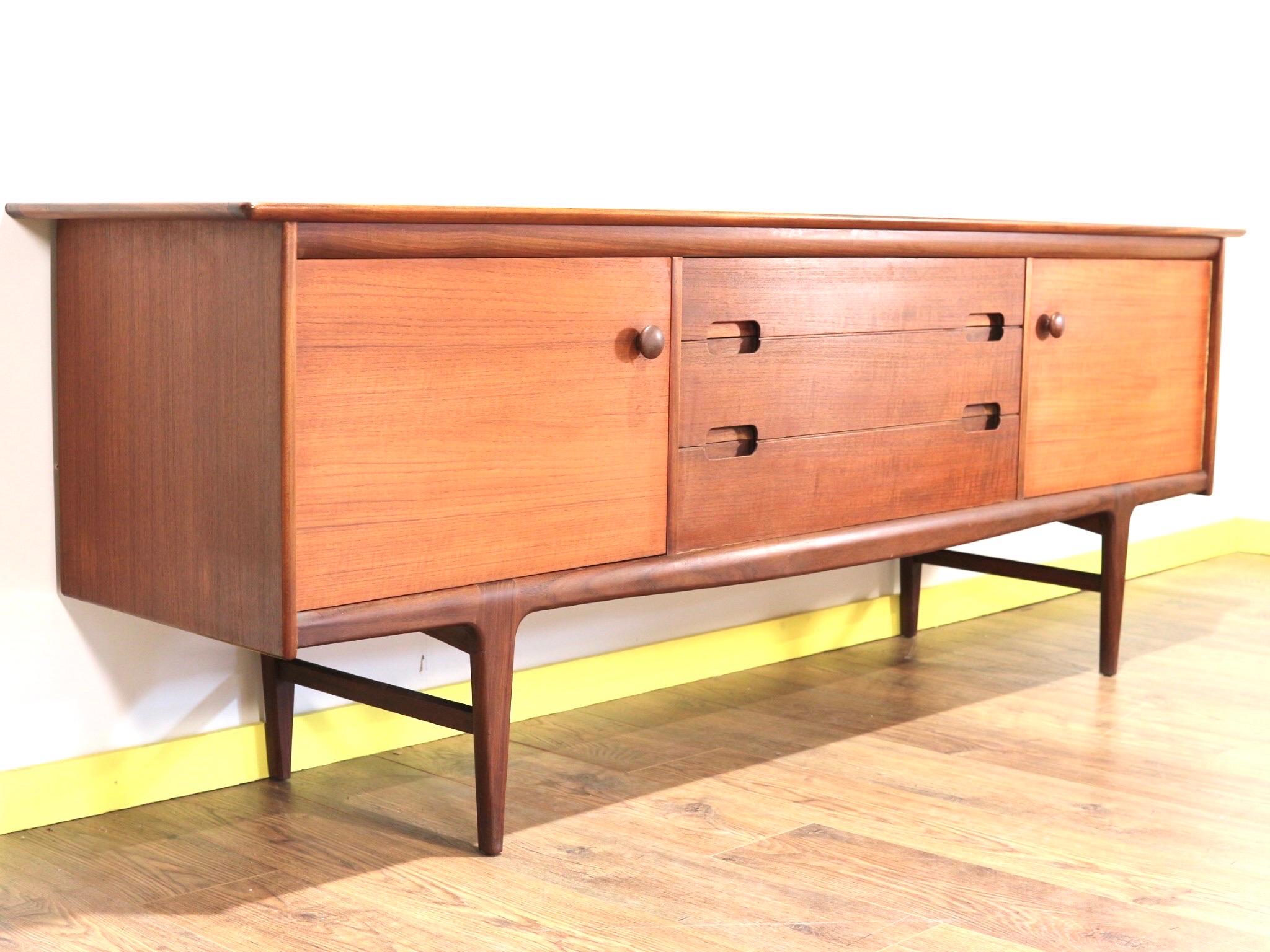 A beautiful teak sideboard by British firm Younger designed by John Herbert in the 1960's. Superbly built with excellent craftsmanship. and stylish handles and legs this is a true statement piece.
A central bank of three drawers flanked by a