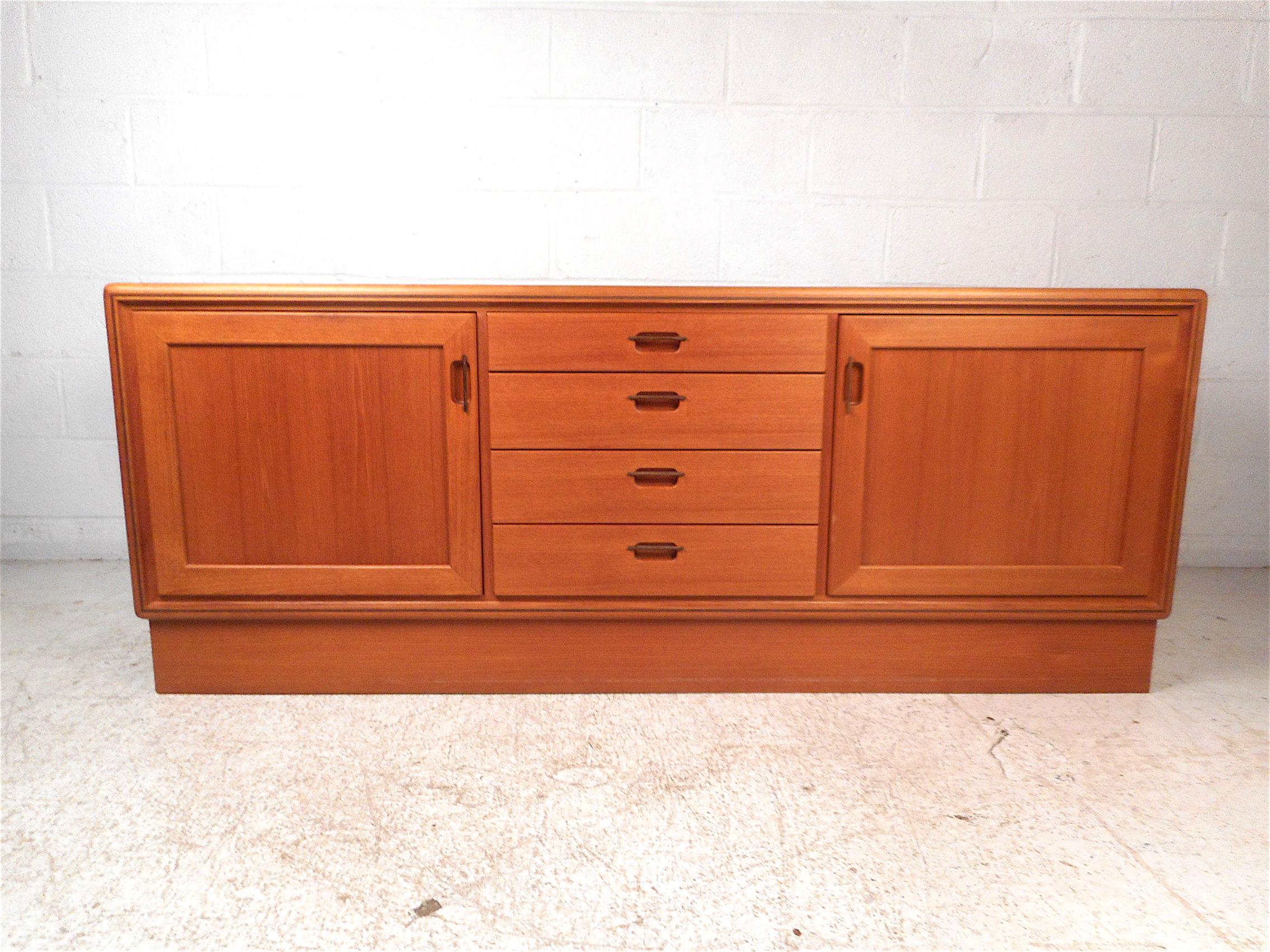 Impressive midcentury credenza. Handsome teak wood grain pattern throughout. Ample storage space, two cabinets on either side with adjustable shelving, four drawers in the center with the upper-most drawer having a felt-lined base, all