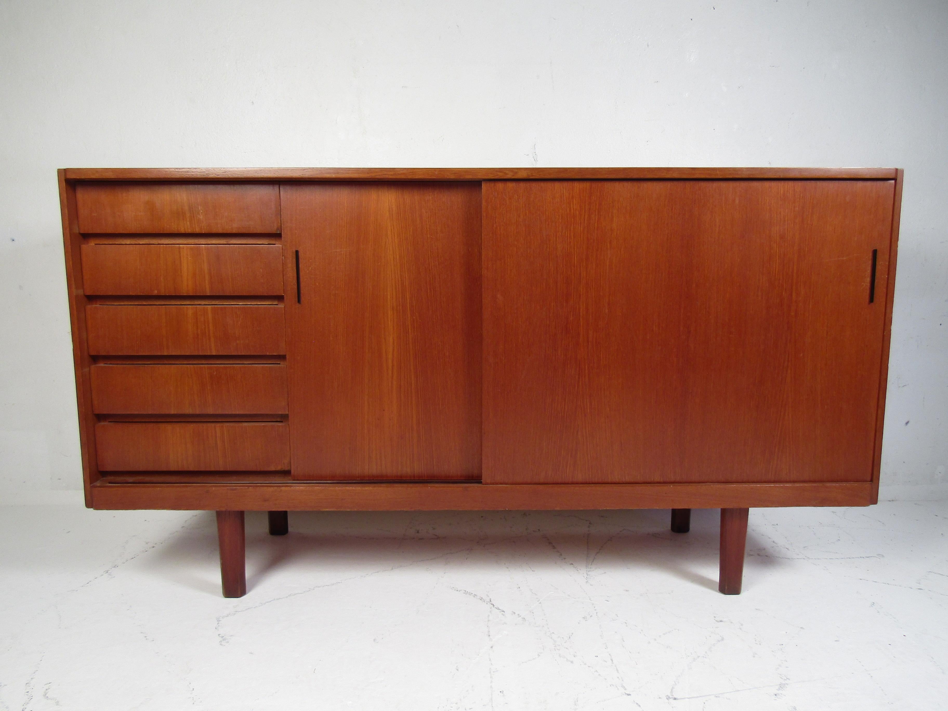 Stylish midcentury teak credenza. Pair of sliding doors which conceal storage space with adjustable shelving. Five dovetail jointed drawers. Great addition to any modern interior. Please confirm item location with dealer (NJ or NY).