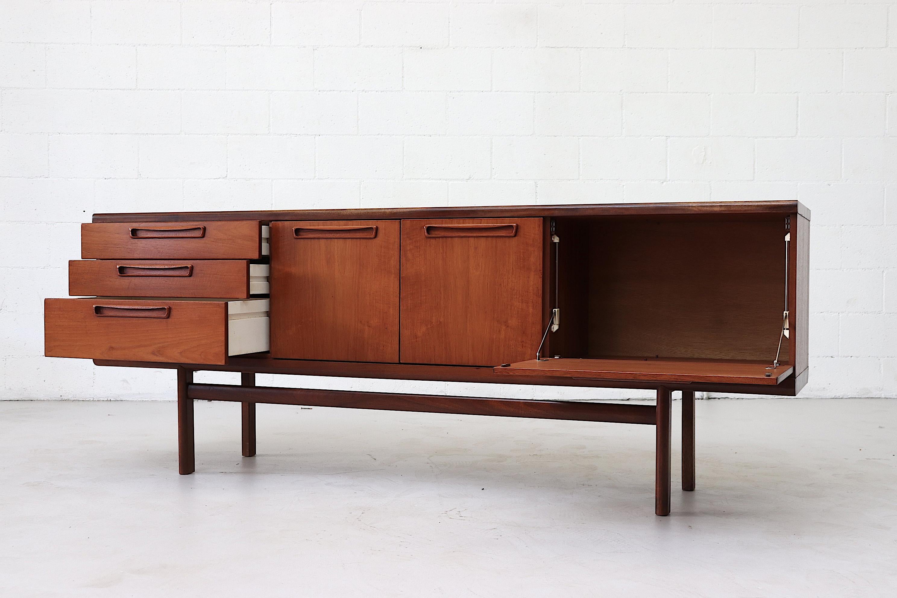 Beautiful midcentury teak credenza equipped with three stacked drawers a centre cabinet with built-in shelf and additional large drop down cabinet. Original condition with light refinishing.
