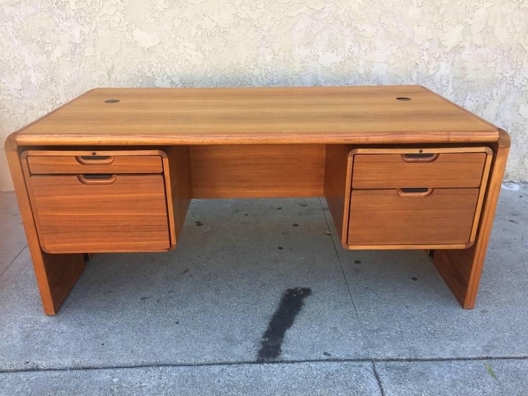 1960s midcentury desk in teak has two larger drawers on bottom that can hold hanging files and two top drawers for smaller objects. There are two holes at the top that can be closed or opened to let through electrical wires. The hardware is in black