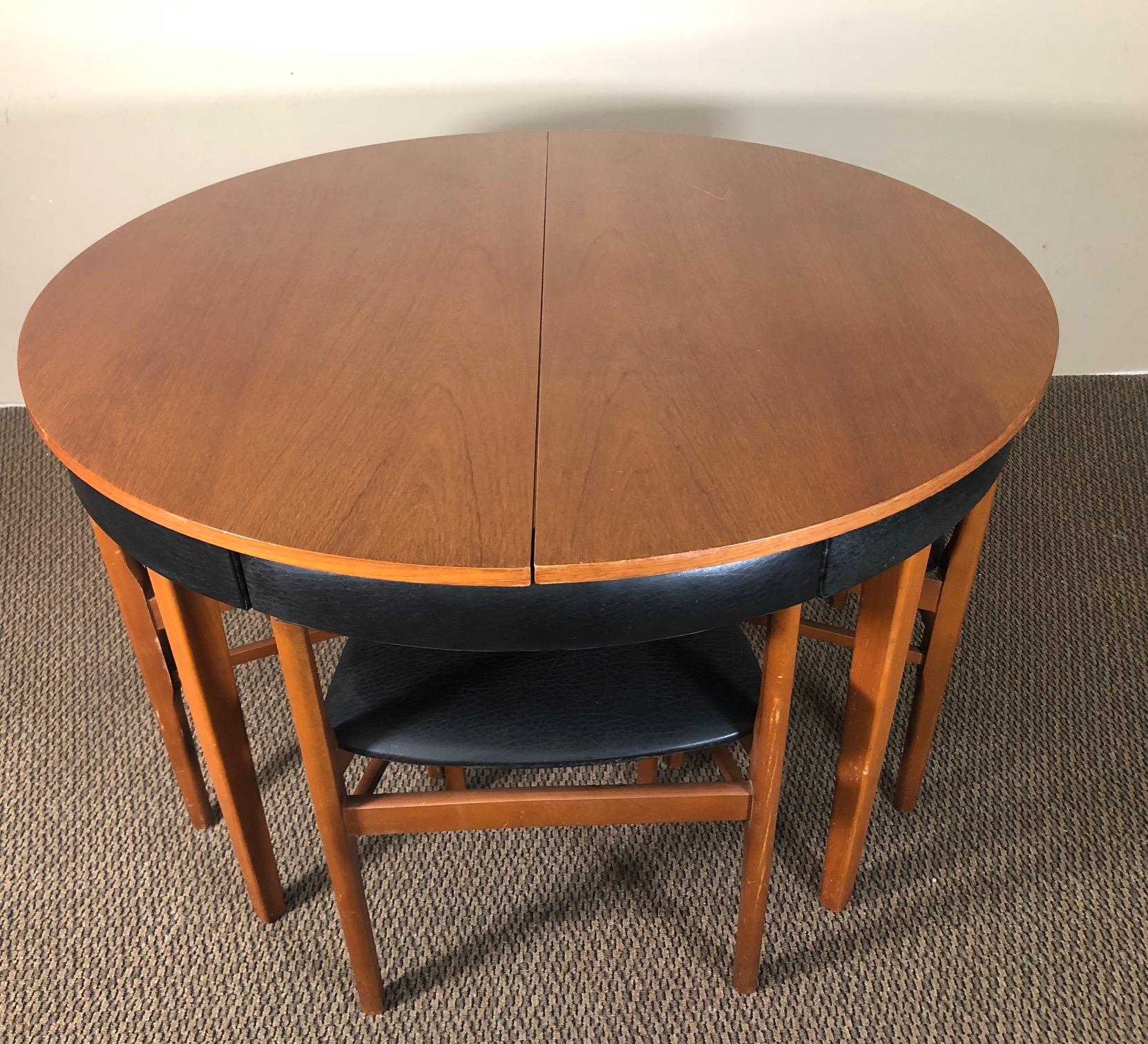 Fantastic midcentury teak dining set similar in style to the legendary Frem Rojle Hans Olsen sets.

Featuring a teak table with pop-up leaf and 4 dining chairs with black vinyl upholstery. The chairs fit perfectly underneath the table when in use