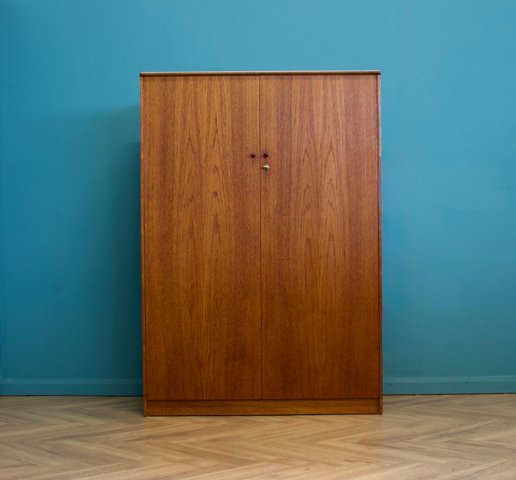 Un armadio freestanding a due ante in teak
Realizzato negli anni '60

Dotato di un appendiabiti per tutta la sua larghezza
Lo stile di questo guardaroba è piuttosto minimalista, con le sue linee pulite.

Maniglie in teak massiccio

Questo armadio è