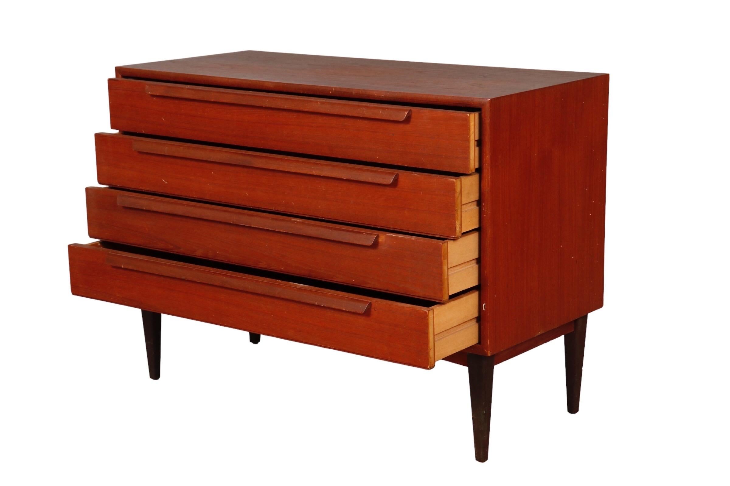 A mid century four drawer dresser made of teak. Each drawer opens with a long applied bar handle. Stands o. Round tapered legs.