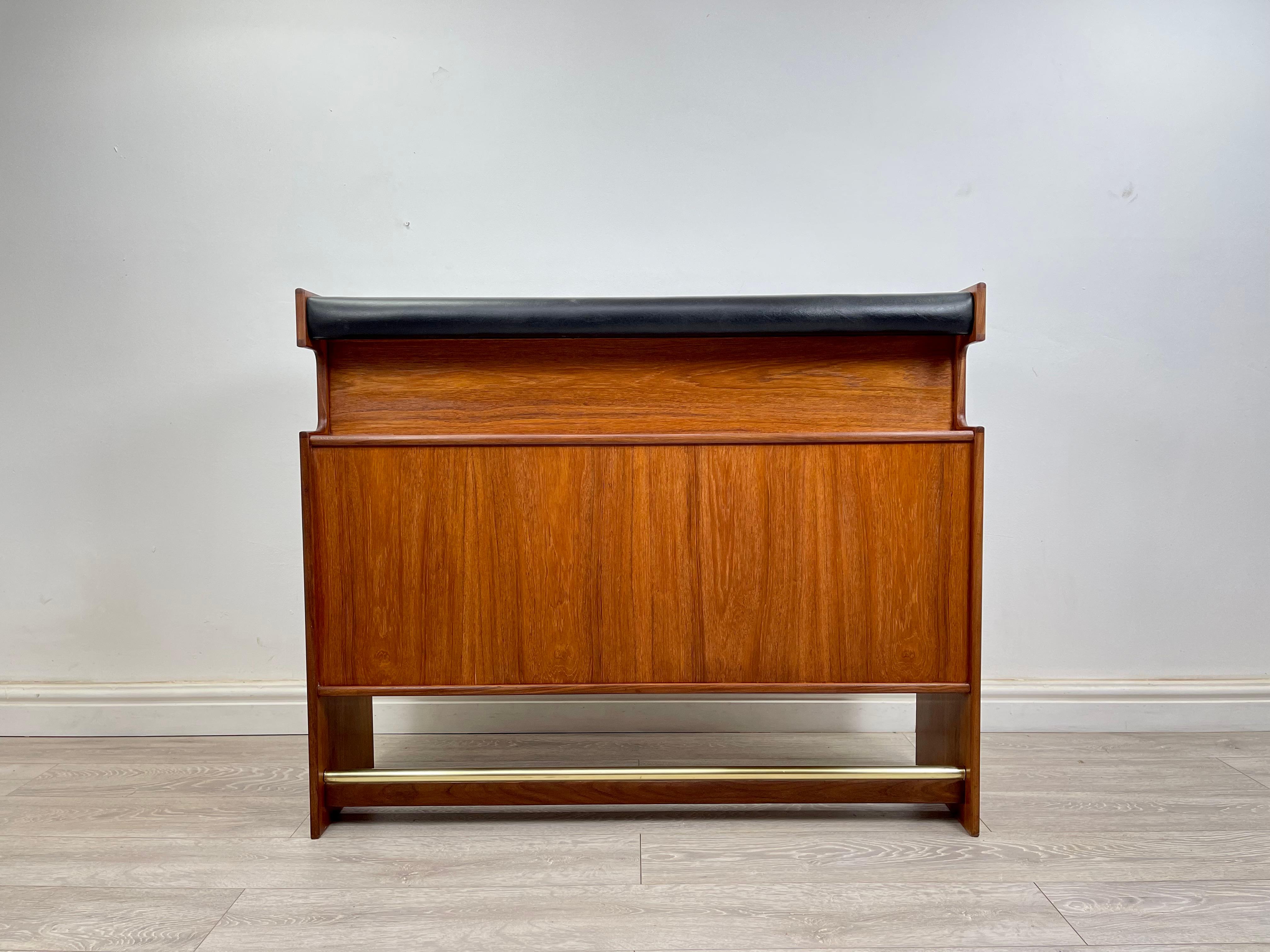 DRINKS BAR 
A stunning mid century teak  drinks bar  circa 1960 . The drinks bar has stunning grain and golden patina throughout , fitted with a brass foot rest and 
black leatherette top rail . 
The  back of the bar has plenty of storage for 