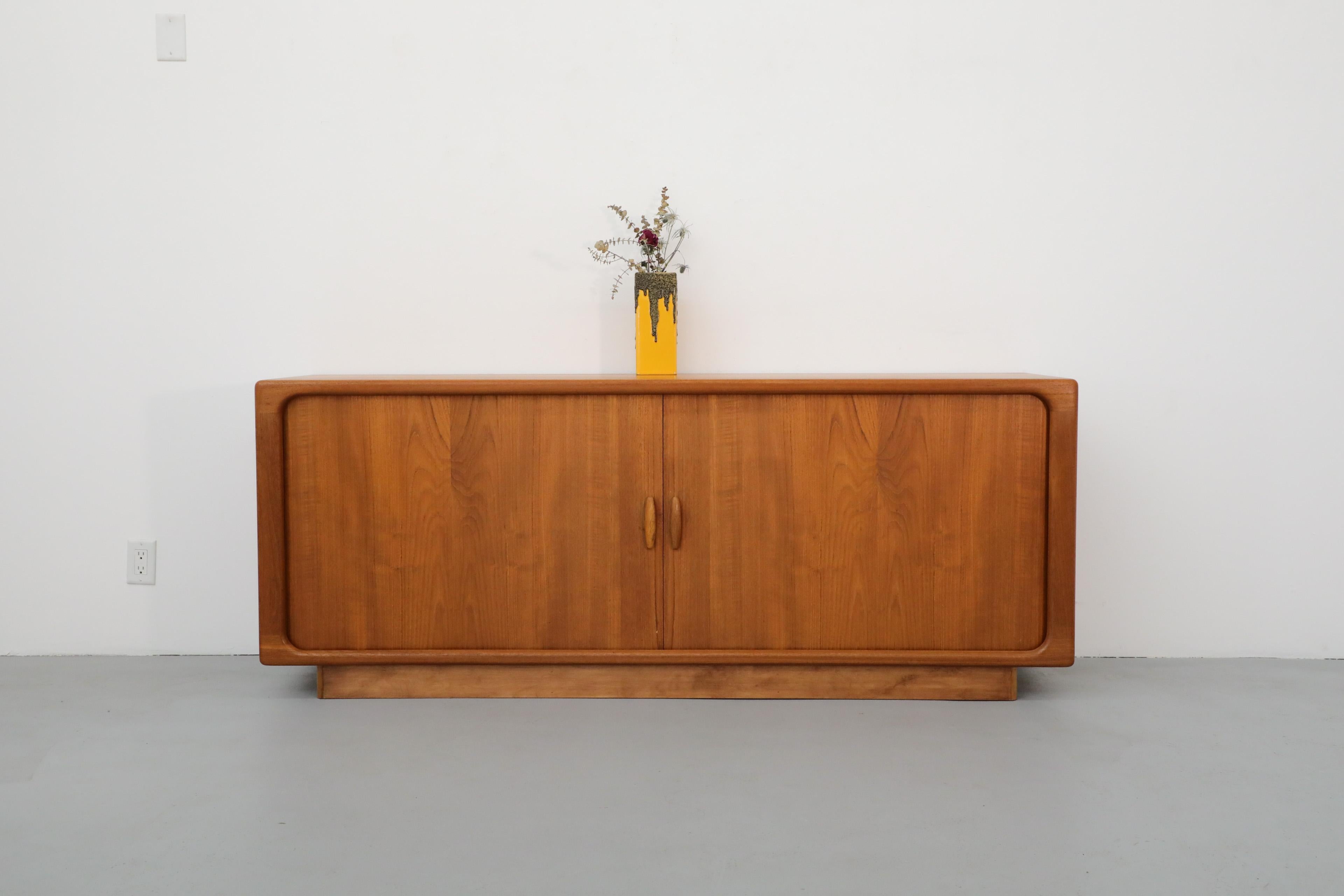 Mid-Century Teak Dyrlund sideboard with two beautiful sliding tambour doors, inner shelves and drawers. This piece has been lightly refinished, a new base was made. Comes with original pamphlet.