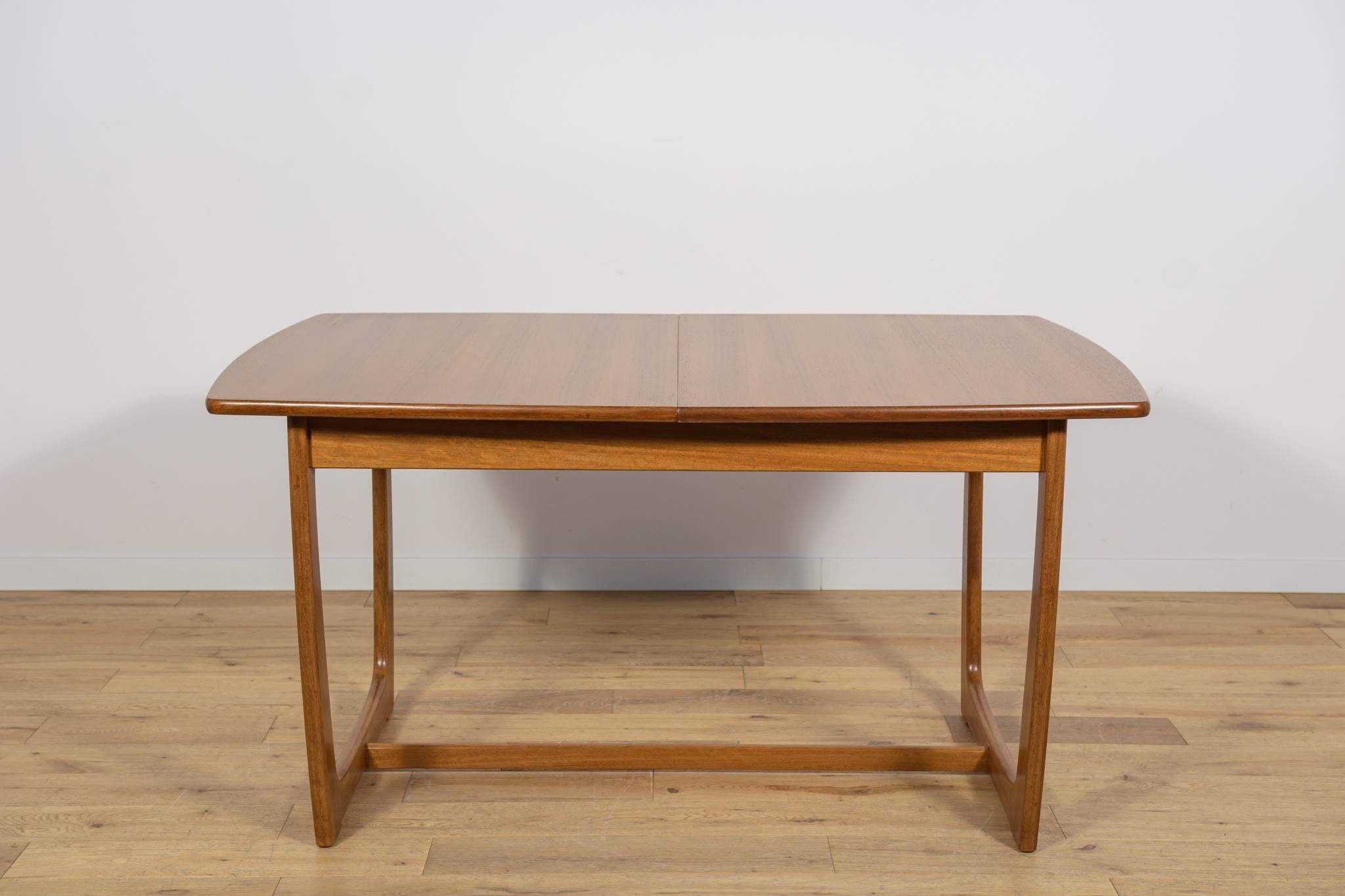 Esta mesa de comedor rectangular extensible fue fabricada por G-Plan en la década de 1960. La mesa tiene los bordes de la parte superior perfilados y reforzados. Elementos de teca limpiados de revestimiento antiguo y pintados con tinte de roble y