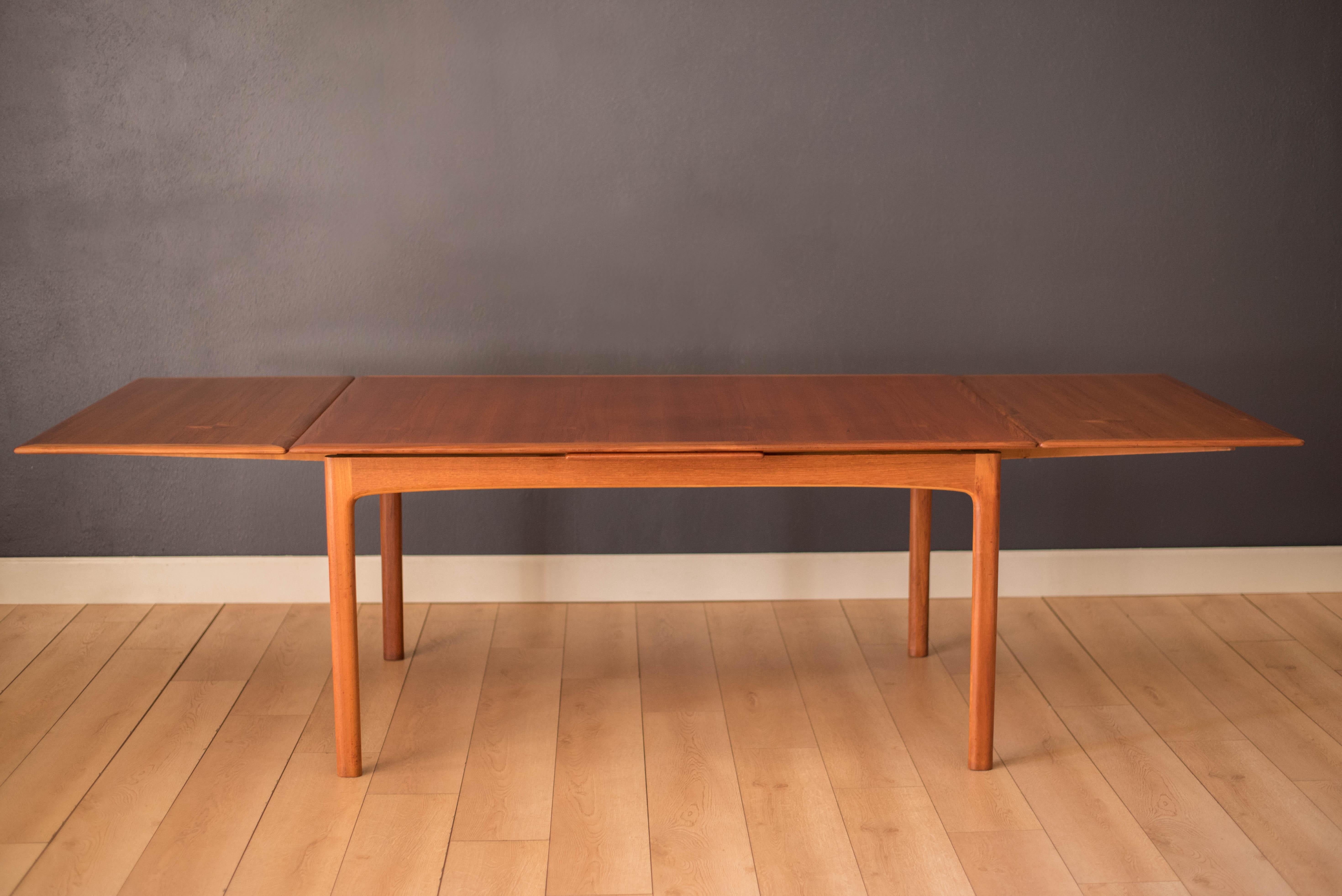 Mid century modern expandable dining table in teak designed by Folke Ohlsson for DUX, Sweden. This versatile piece includes two draw leaf extensions that cleverly store underneath the table. Features a vertical teak grain pattern framed with wide