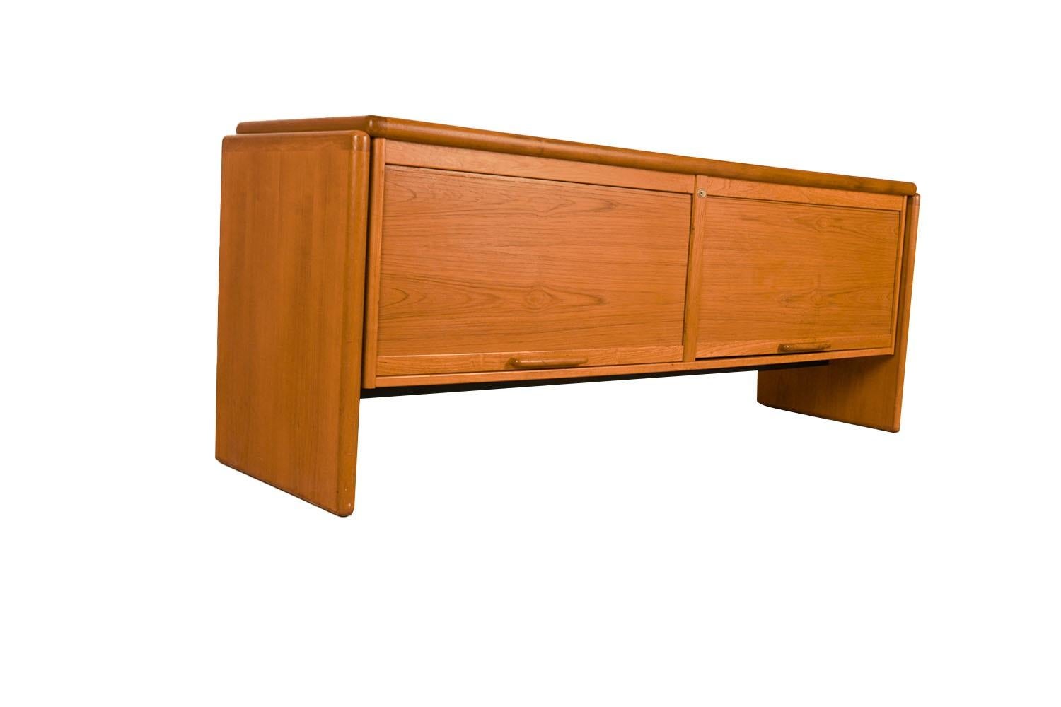 An exceptional teak file cabinet/credenza, circa 1970’s, made in Denmark, by Dyrlund. This absolutely stunning piece features two sliding Vertical Tambour Doors that open to reveal a finished interior with a large sliding file deep drawer on the