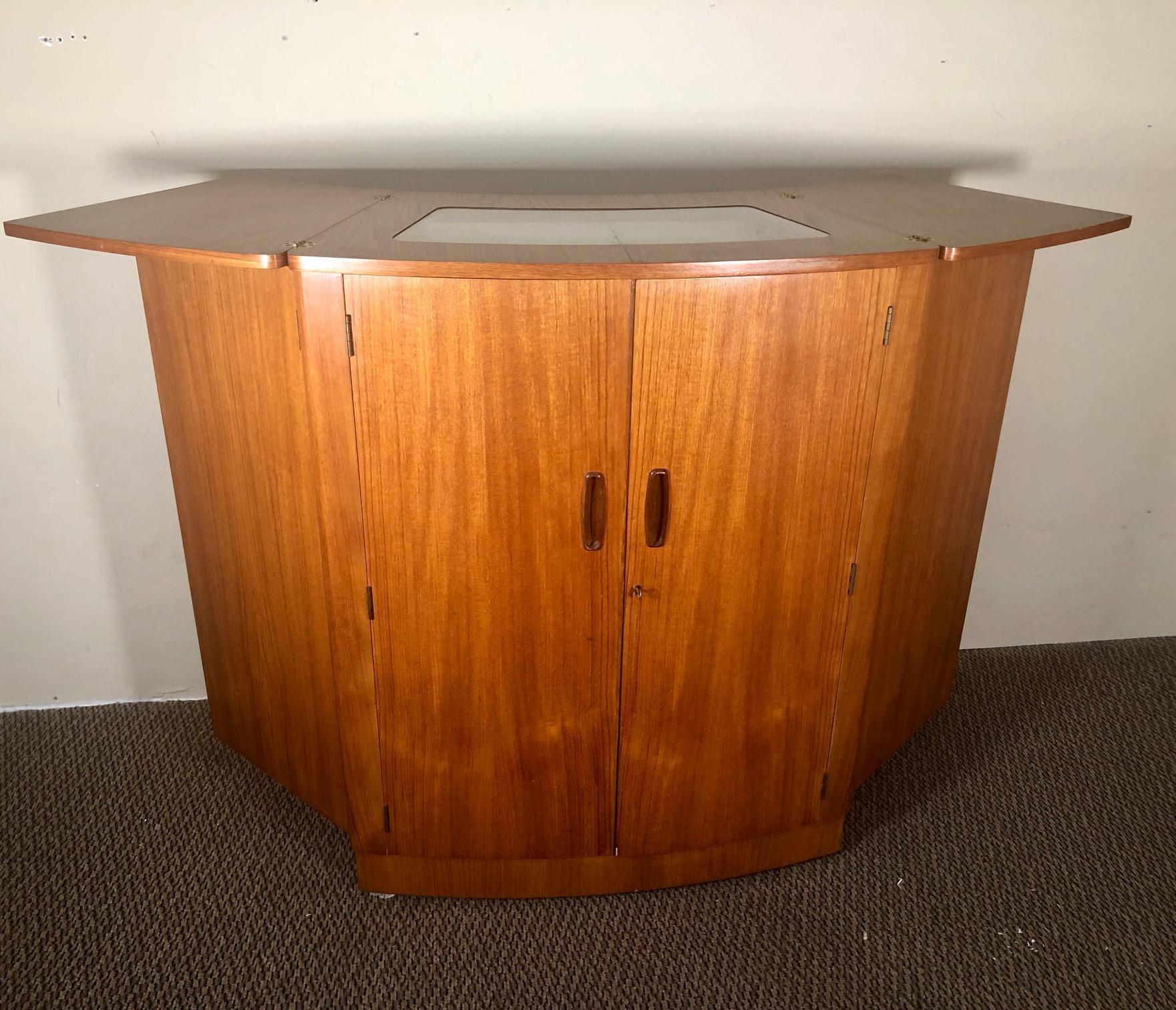 This is a gorgeous space saving midcentury teak bar by Turnidge of London. The top unfolds and the sides fold out. The bar is on wheels.
Excellent vintage condition. Some of the orignal accessories are missing. The metal clips in the doors used to