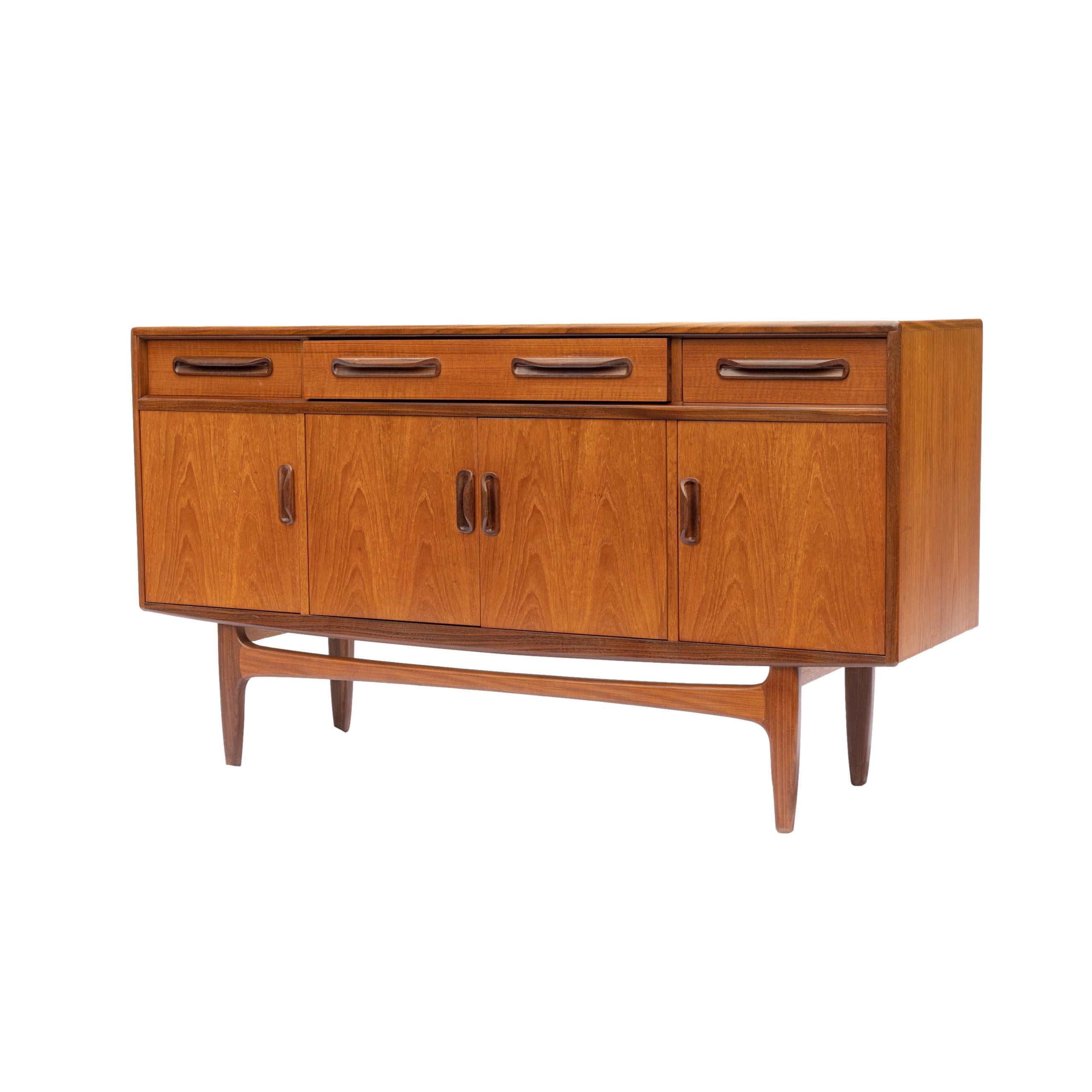 Mid-Century Modern teak Fresco sideboard designed by Victor Wilkins for G Plan, English, ca. 1960, with three frieze drawers, one long with fitted interior and two short, above four open cabinet doors; all with molded sculptural handles, on a Danish