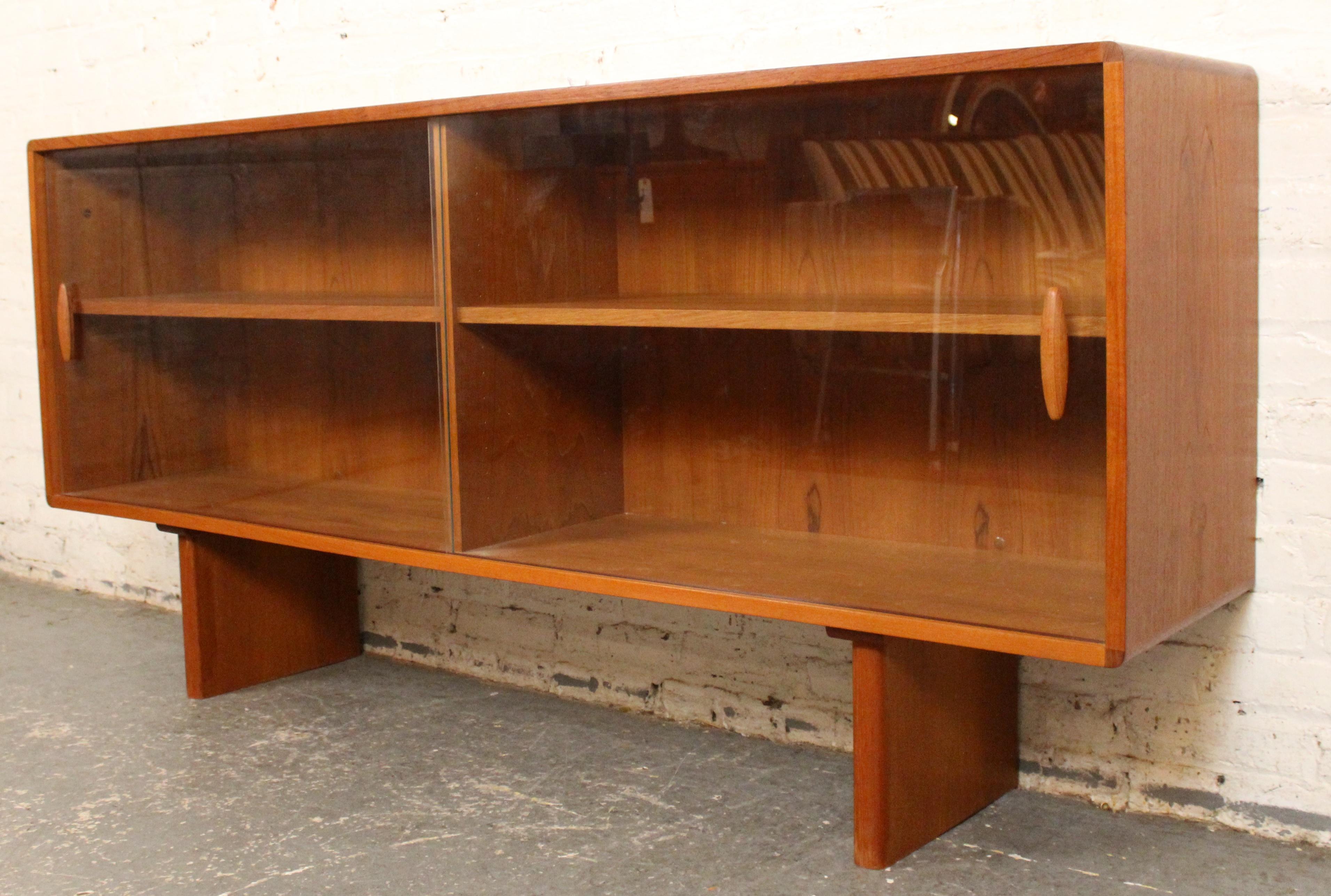 Elegant and functional, this Mid-Century bookcase topper by Dyrlund features rich teak wood and sliding glass doors. Crafted in Denmark, it showcases the clean lines and timeless design characteristic of Scandinavian modernism. Perfect for