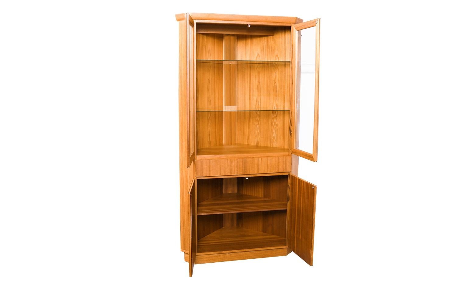 This stunning corner cabinet is a beautiful example of Danish modern furniture by Skovby Mobelfabrik. The lighted one piece cabinet features an upper cabinet with double glass doors that open to reveal a lighted display area at top, with a single