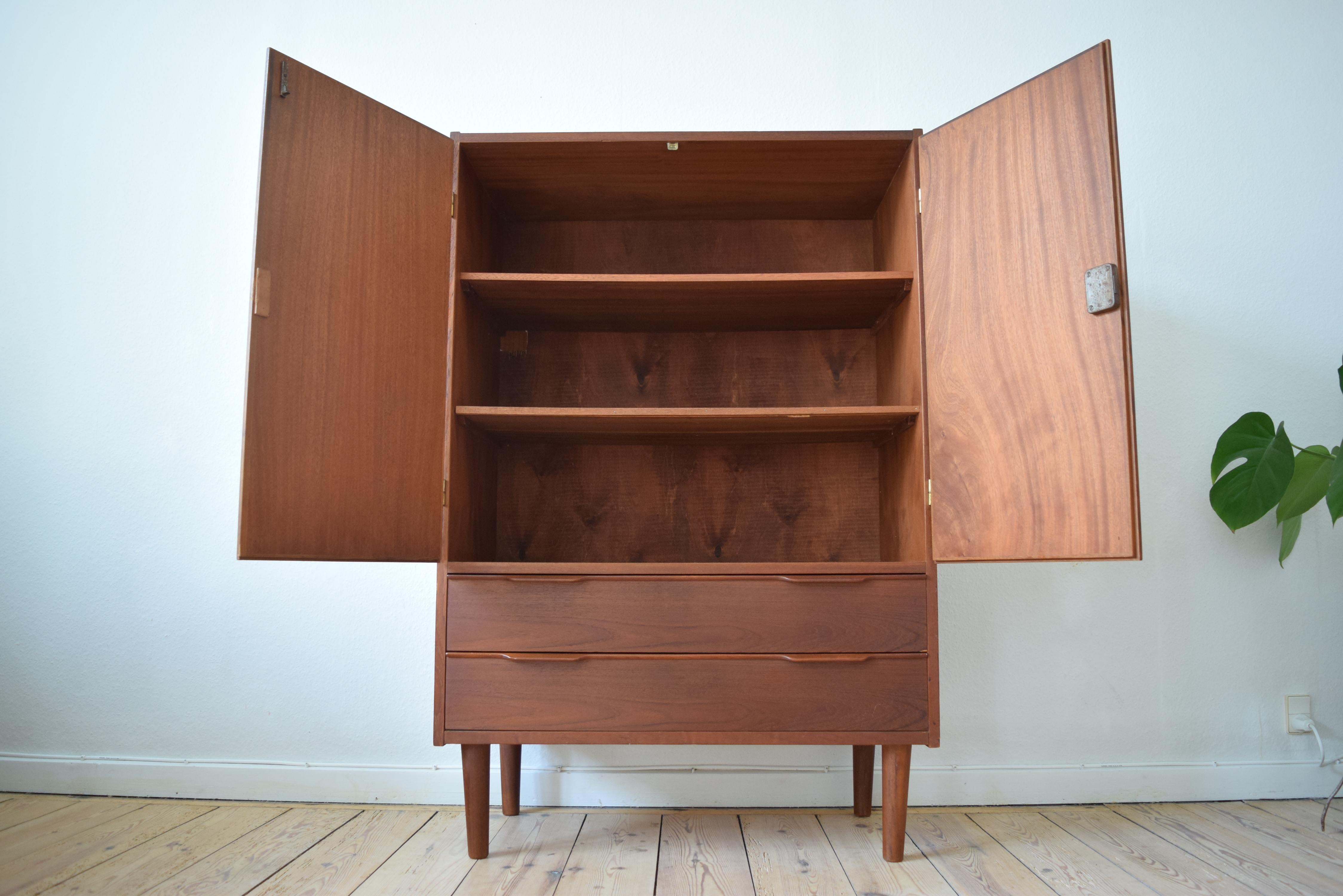 High sideboard manufactured in Denmark in the 1960s. Features two drawers and two lockable doors (key included) with shelves. Sits on tapered teak legs. Previous interior ducting hole has been covered with a teak plate.