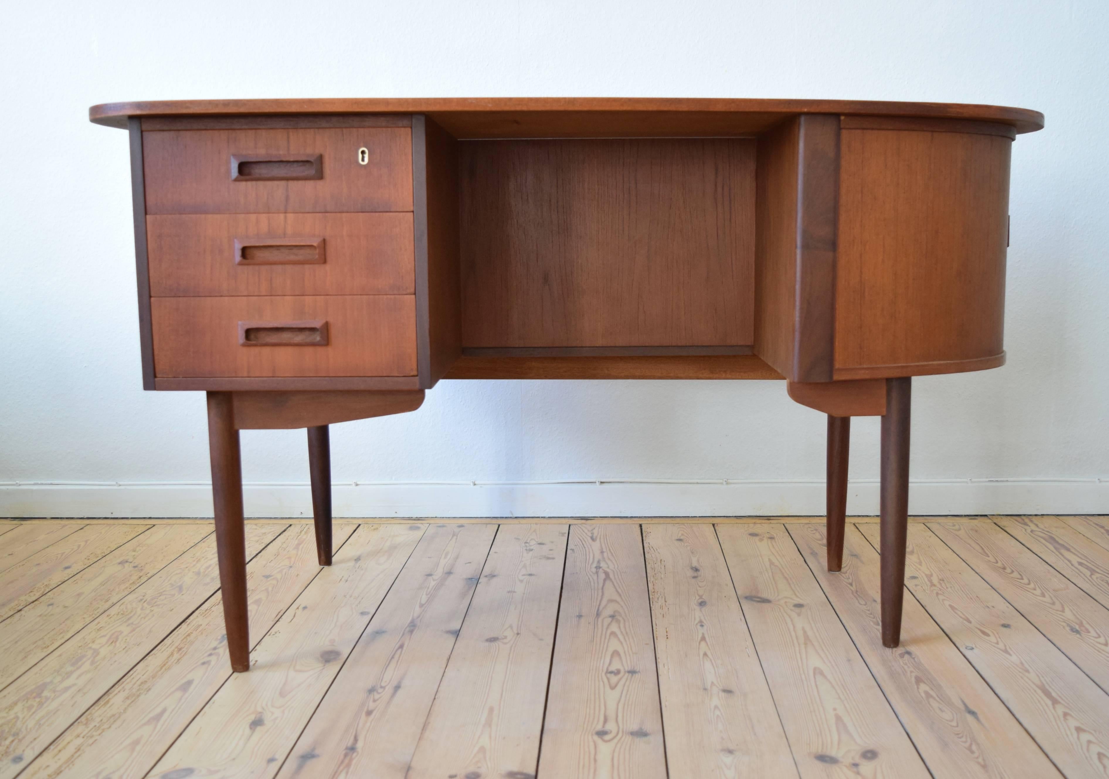 Teak desk manufactured in Denmark in the 1950s featuring an organic kidney shape top plate, bar with tambour door, bookshelf on the back and three drawers one lockable. Apart from a few marks here and there on the top plate this item is in good