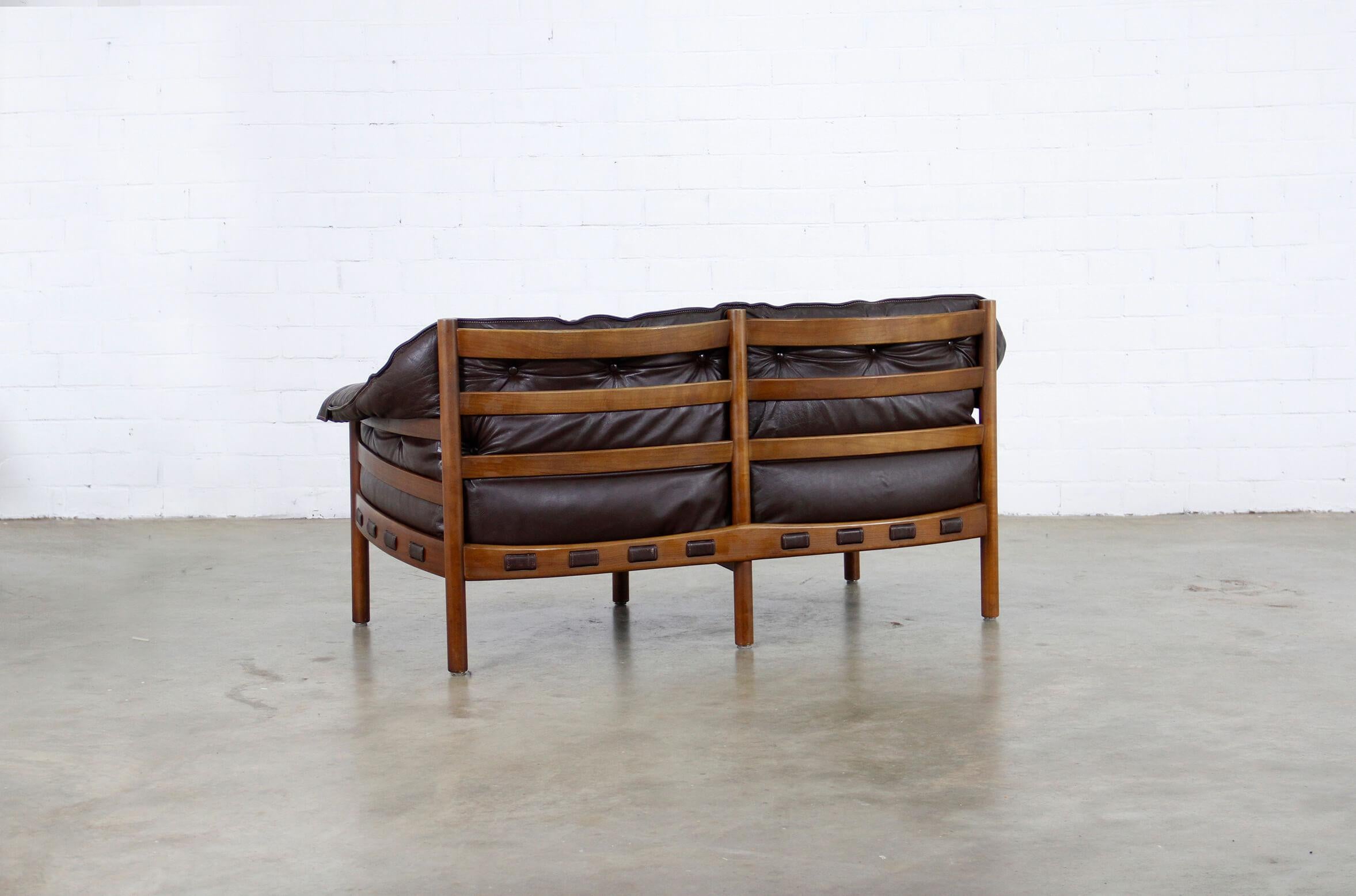 This sofa dates from the 1960s. It features cushions upholstered in dark brown leather and a frame in teak.
 