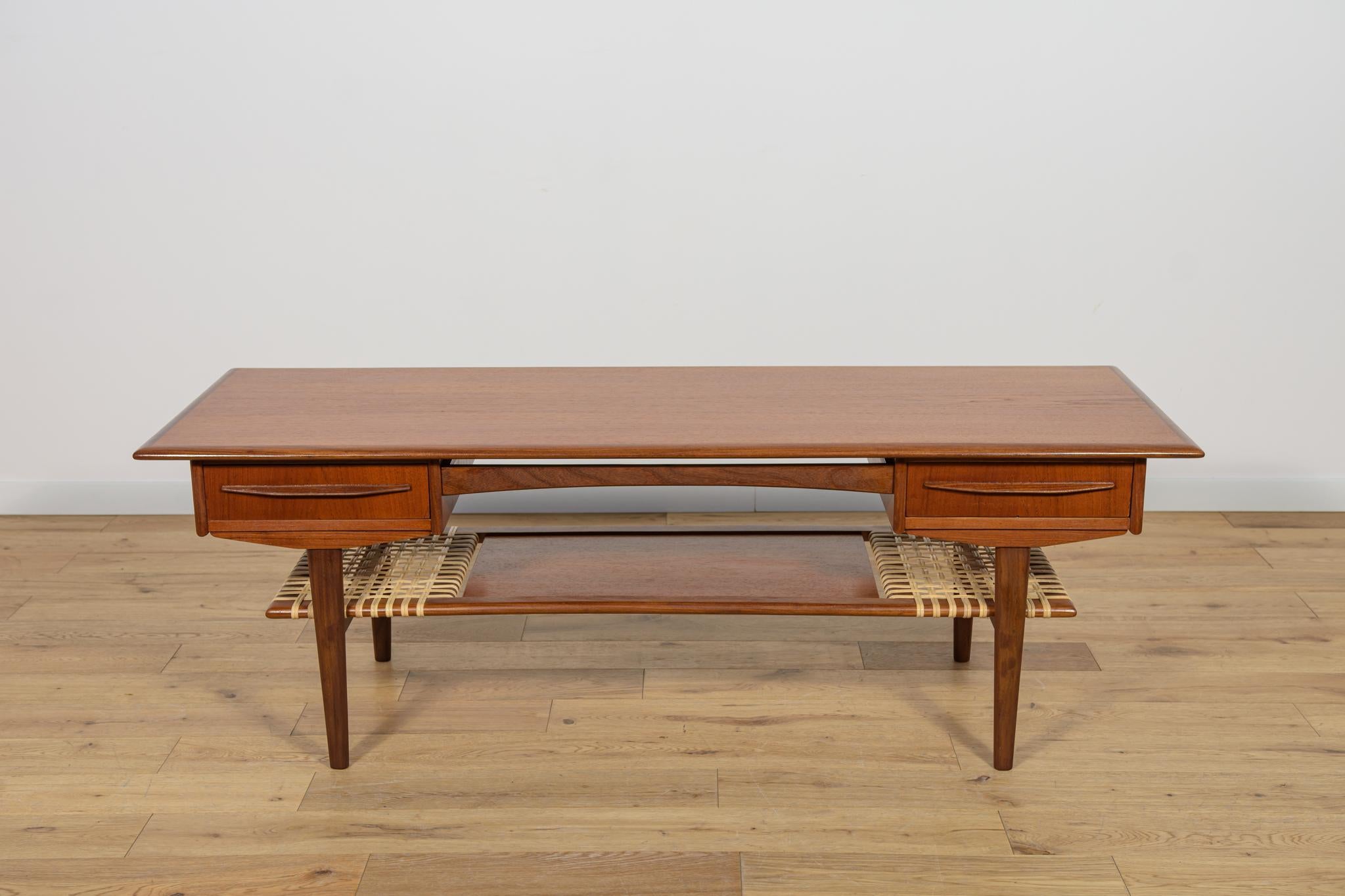 Table basse fabriquée au Danemark dans les années 1960. Fabriqué en teck. Tablette inférieure en rotin tressé. Sous le plan de travail supérieur, deux tiroirs s'ouvrent des deux côtés. La tablette supérieure a des bords solides profilés. Table basse