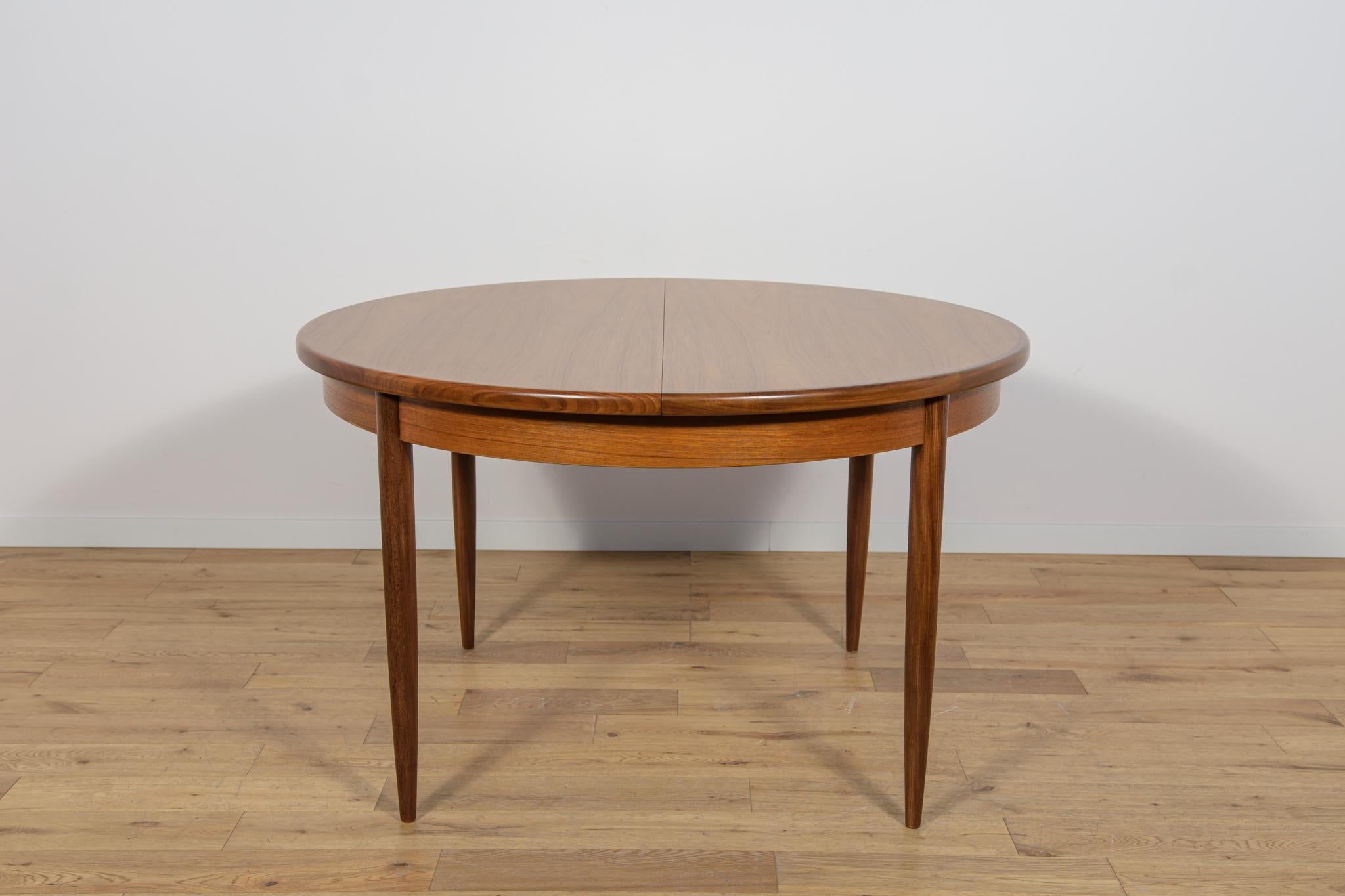 Esta mesa de comedor redonda extensible fue fabricada por G-Plan en la década de 1960. La mesa tiene los bordes de la parte superior perfilados y reforzados. Elementos de teca limpiados de revestimiento antiguo y pintados con tinte de roble y