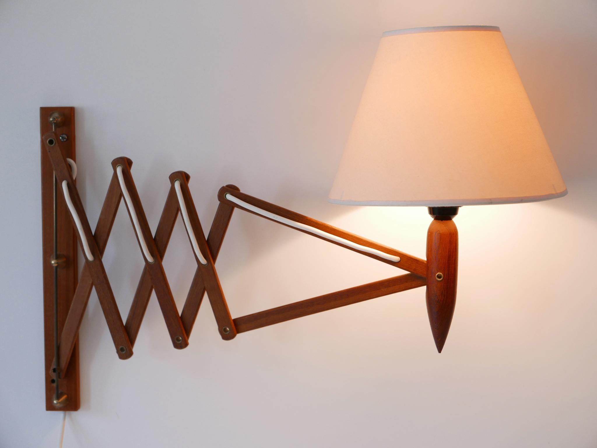 Elegant Mid-Century Modern teak scissor wall lamp. Designed by Erik Hansen for Le Klint, Denmark, 1960s. 

Executed in teak wood and fabric, the wall lamp is executed with  1 x E27 / E27 Edison screw fit bulb socket. It is wired, and in working