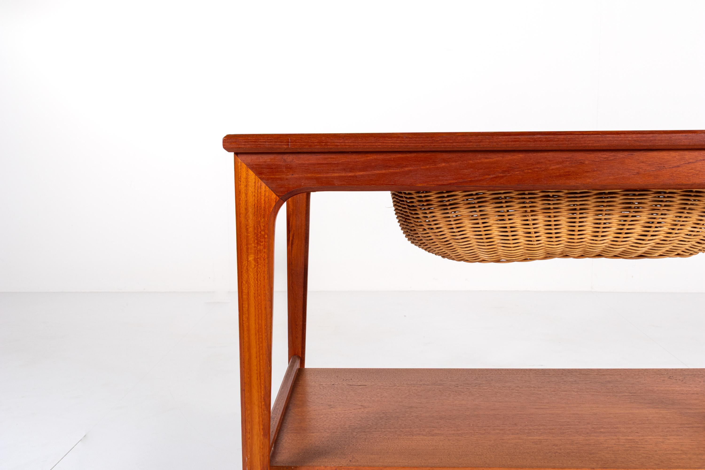 This mid-century teak trolley, originally crafted for textile arts like knitting or sewing, offers versatile functionality as a bar cart or side table. It features a sliding rattan basket with a tool shelf tucked beneath the tabletop, a lower shelf