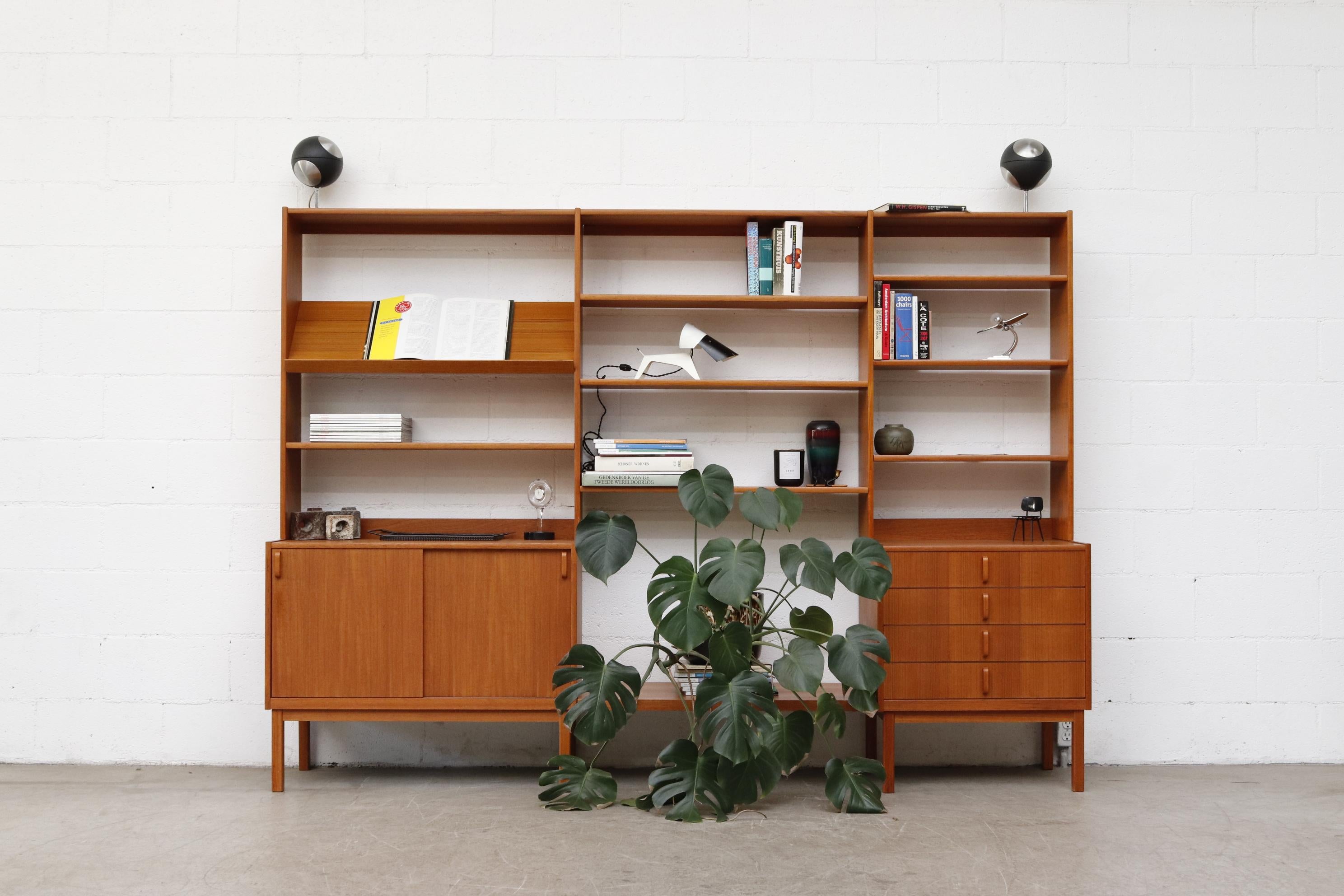 Handsome 3 section teak wall unit with 2 lower cabinets and upper shelving, signature colored interior accents. The open lower center area was for what was once used to house a television set. Perfect for large art books, ceramics, or your pet :)