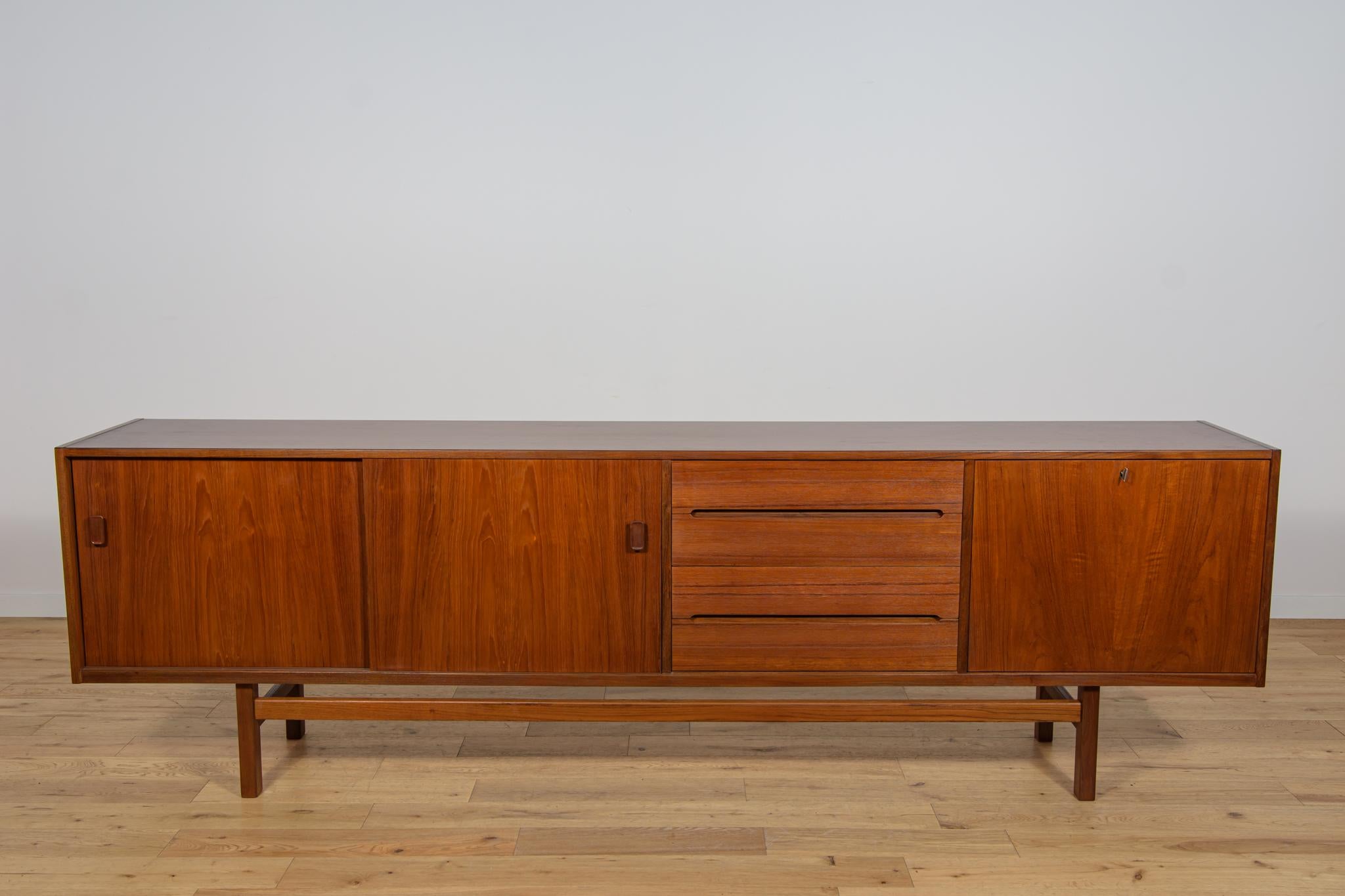 This mid-century Swedish designed long sideboard was designed by Nils Jonsson and manufactured by Hugo Troeds. It is made of teak and features  cabinet with two sliding doors on the left,the middle in they find four drawers and right side is bar.