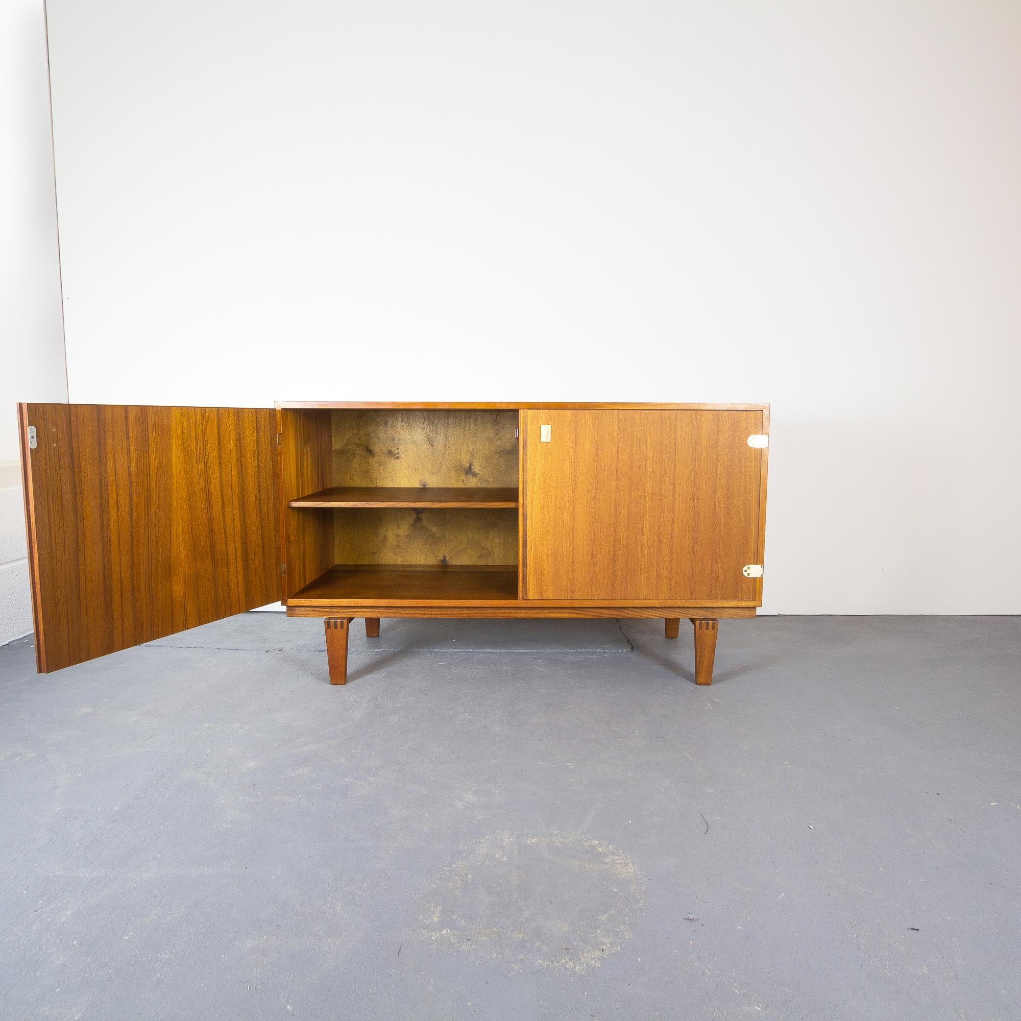 Elegant, small teak sideboard designed by Peter Løvig Nielsen for Løvig, Denmark 1960s. The teak is in great condition and has been fully refurbished. Two hinged doors with brass details. The feet have beautifully crafted dovetail joints. Inside