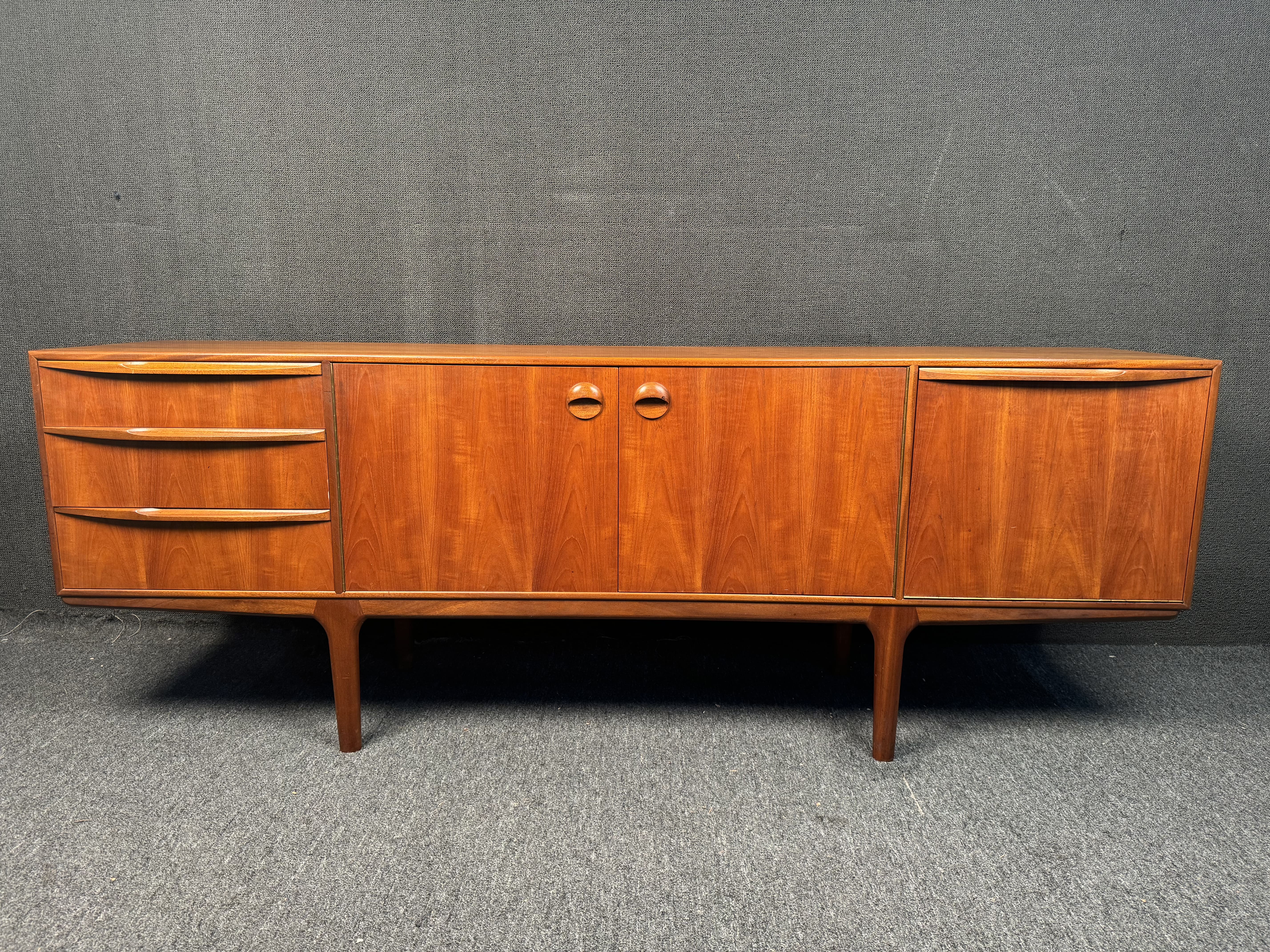Questa credenza di metà secolo in teak, disegnata da Tom Robertson, è stata prodotta in Gran Bretagna da Mcintosh negli anni Sessanta. La credenza ha tre cassetti situati sul lato sinistro, al centro c'è un mobile, sul lato destro c'è una barra e un