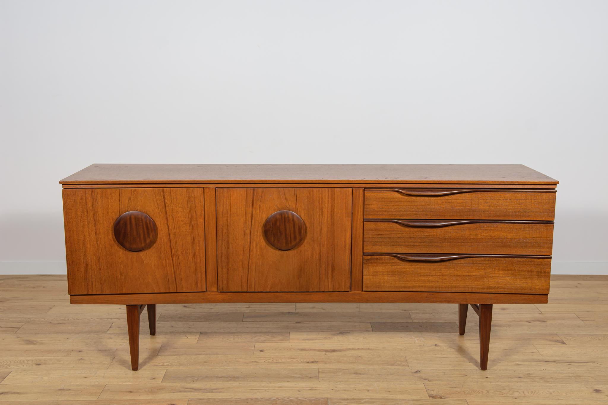 In den 60er Jahren in der britischen Beautility-Fabrik hergestelltes Sideboard. Das Sideboard hat drei Schubladen, eine Bar und einen Schrank. Die Kommode hat eine leichte Form mit interessant profilierten Griffen. Die Möbel wurden einer umfassenden