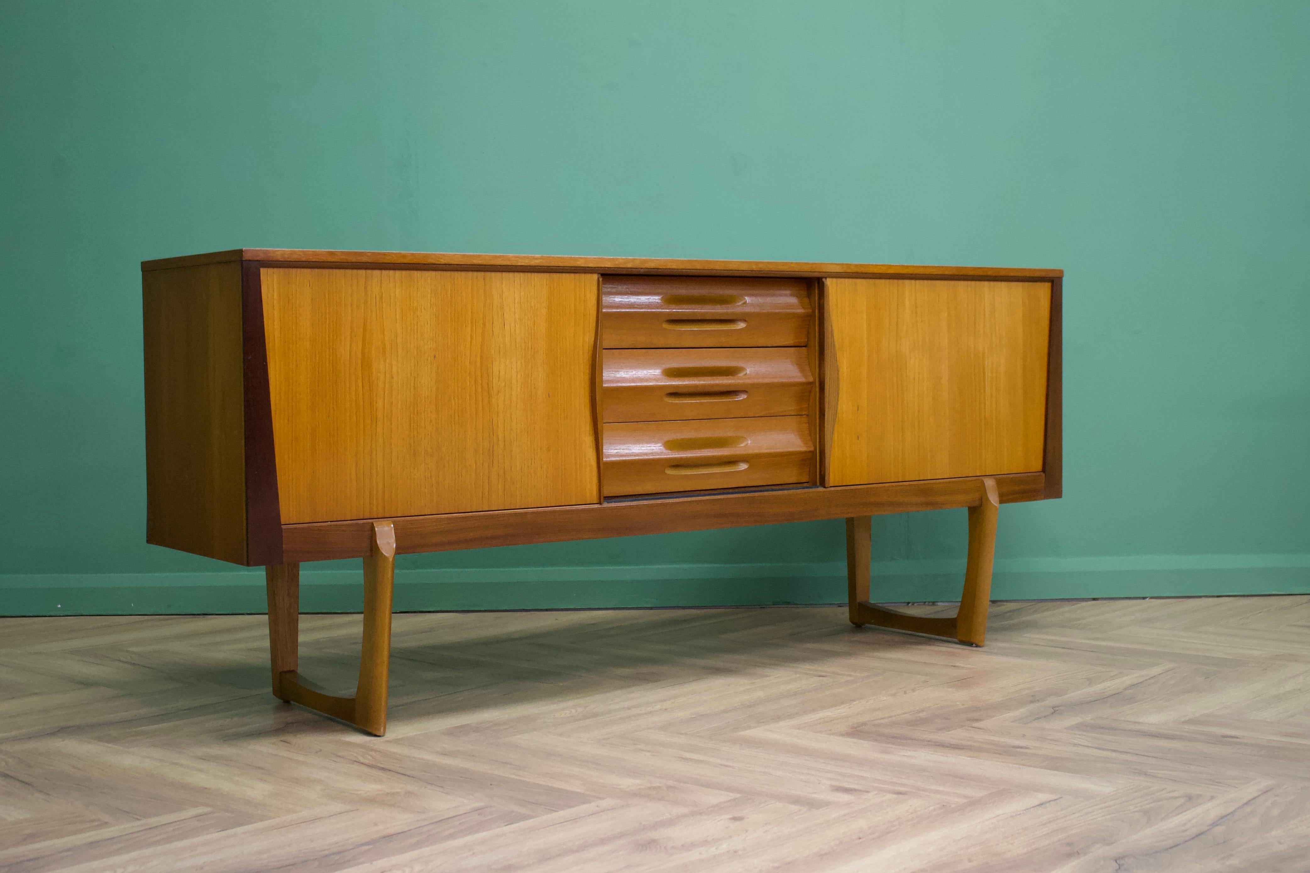 - Mid-Century Modern sideboard.
- Featuring three drawers and two sliding door cupboards
- Manufactured in the UK by Elliots of Newbury
- Made from teak and teak veneer.