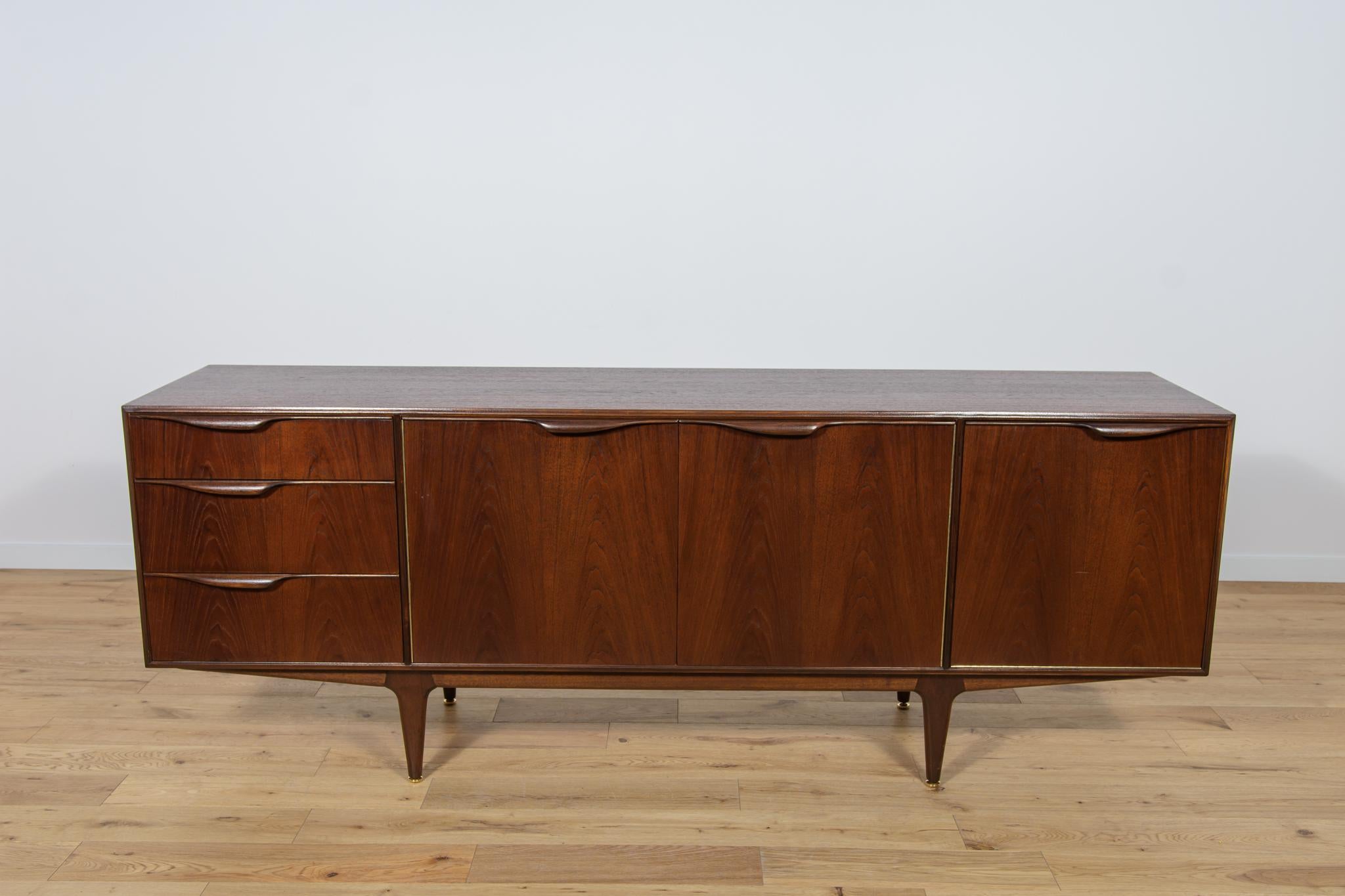 This mid-century sideboard in teak was produced in Great Britain by Mcintosh in the 1960s. The sideboard has three drawers and a cabinet, on the right side there is a bar with  pull-out top. Sideboard made of teak wood with profiled handles. The
