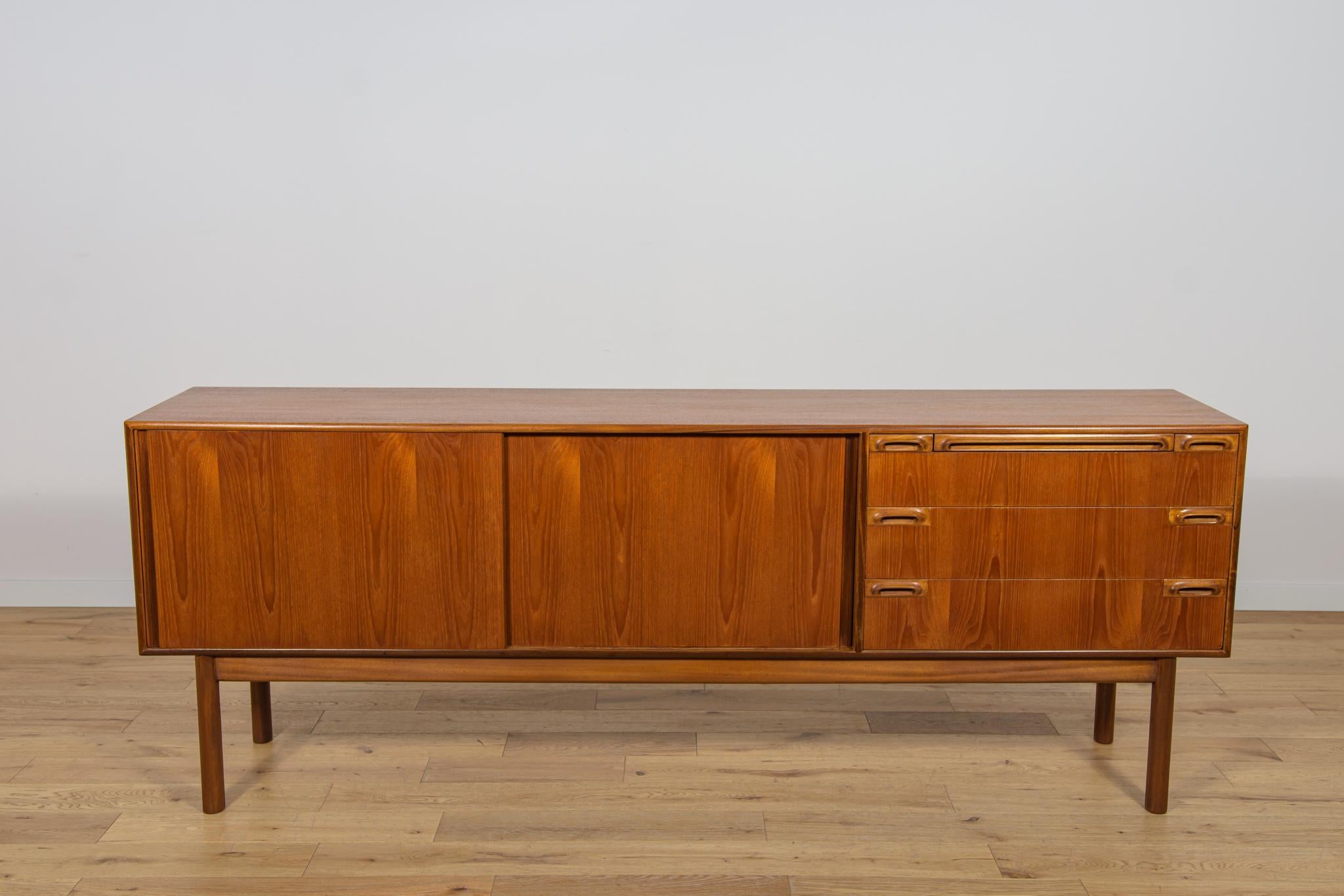 Das Sideboard wurde in den 1960er Jahren in der britischen McIntosh-Fabrik hergestellt. Das Sideboard hat drei Schubladen und eine ausziehbare Platte mit profilierten Griffen, die auf der rechten Seite platziert sind, auf der linken Seite gibt es