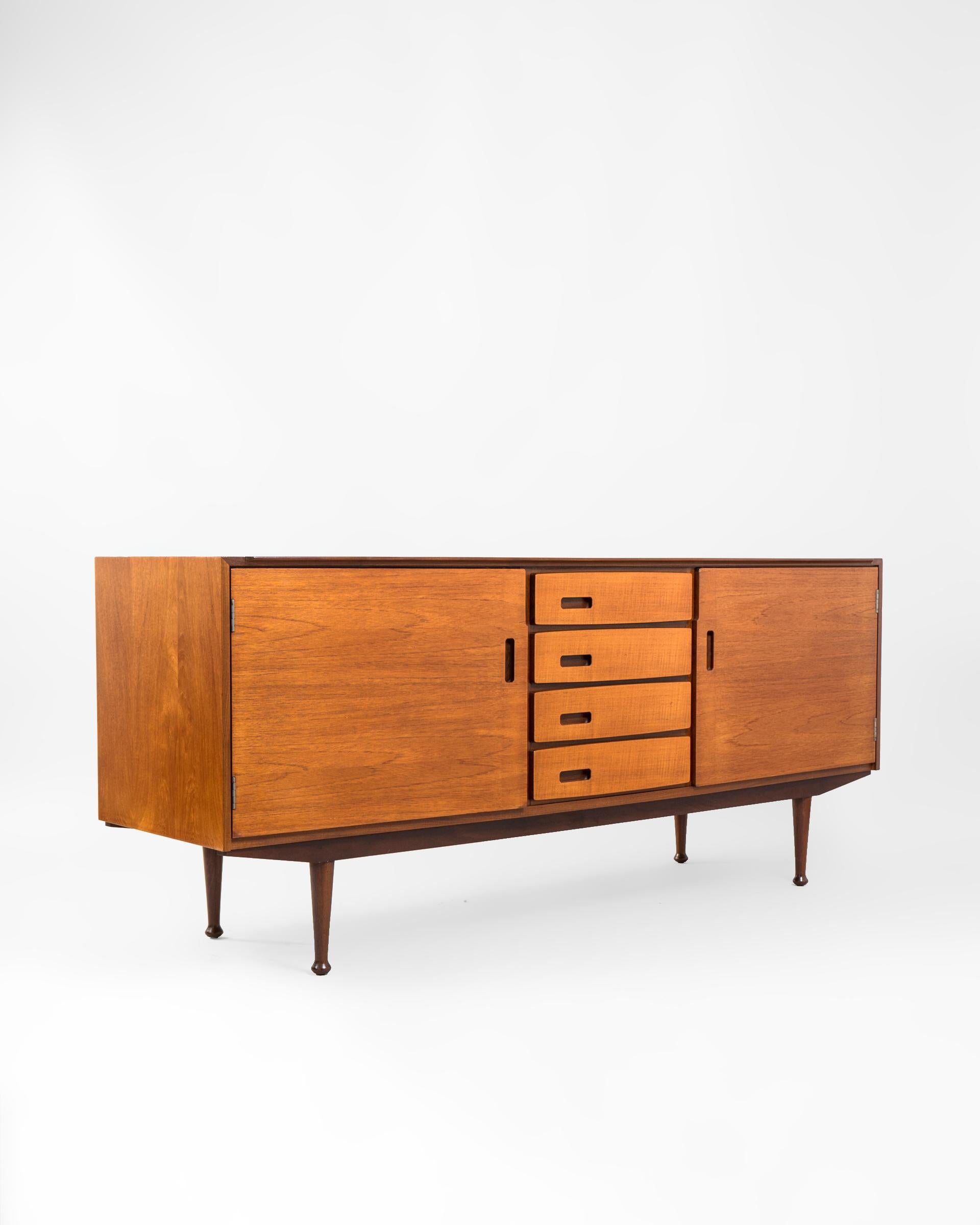 Aparador Mid Century en madera laminada de teca original de la firma inglesa Meredew Furniture Ltd. El diseño se construye simétrico con un armario a cada lateral y un bloque central de cuatro cajoneras. El armario de la izquierda se divide con una