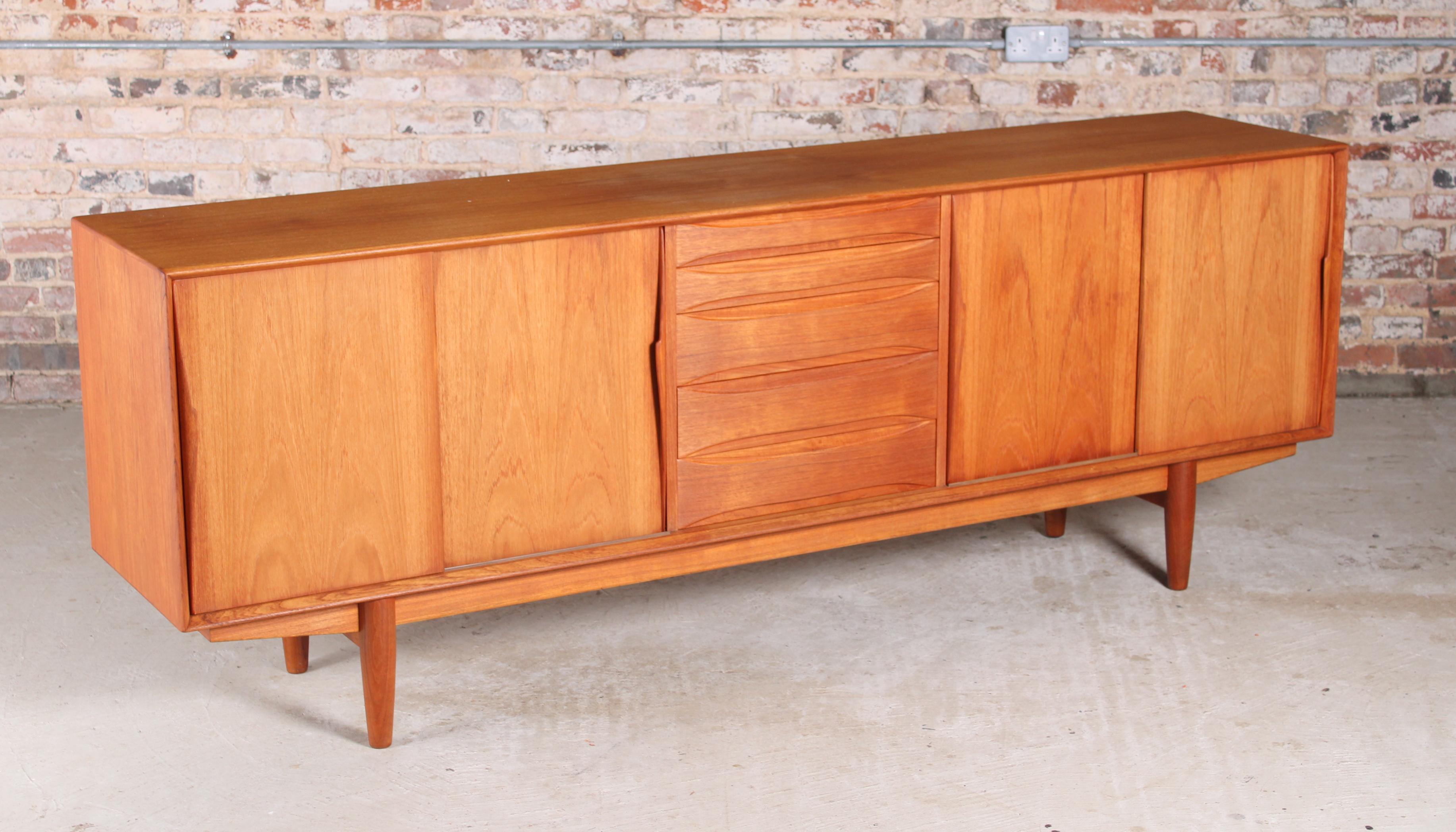 Large mid-century teak sideboard in the manner of Arne Vodder by Dyrlund, Denmark, circa 1960s. 5 drawers and 2 cabinet sections. Sliding doors with carved teak handles.